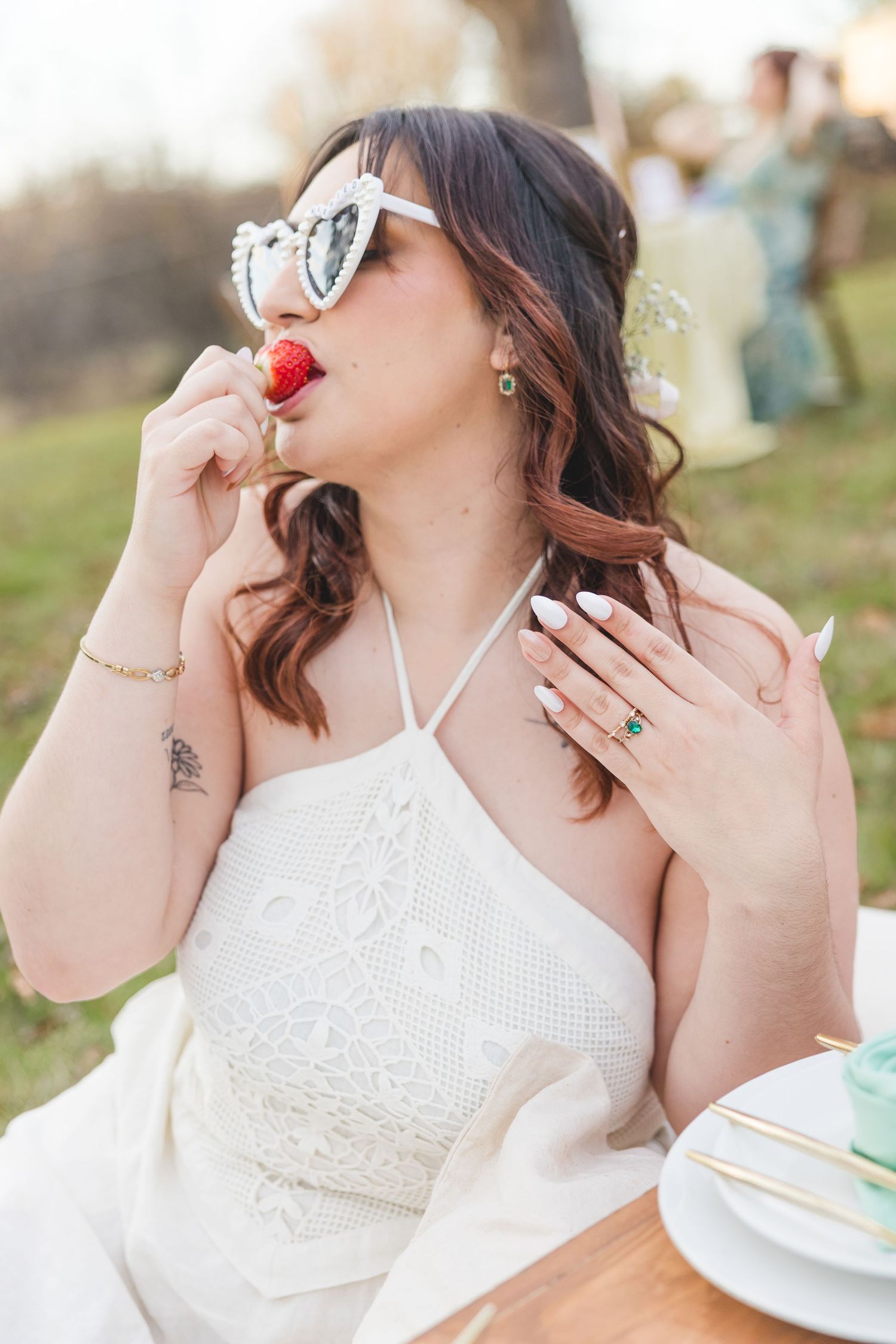 A person in a white lace dress sips from a teacup during an elegant outdoor tea party setting.