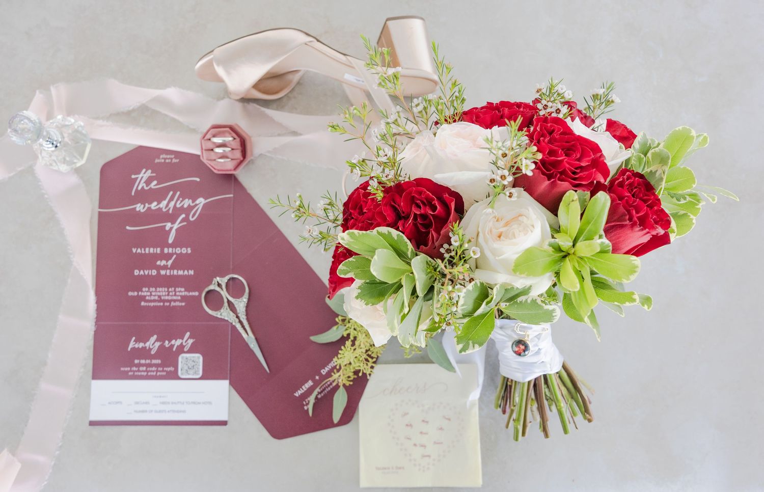 Wedding stationery flat lay with red floral bouquet and mauve invitation cards.