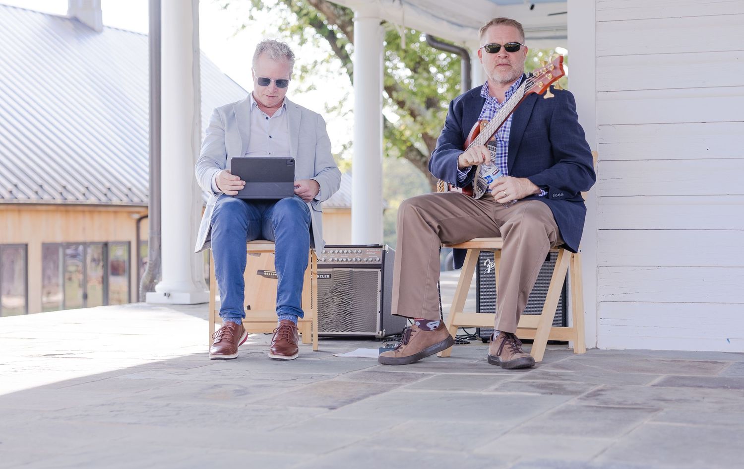 Two men relaxing in rocking chairs on a white porch with electronic devices.