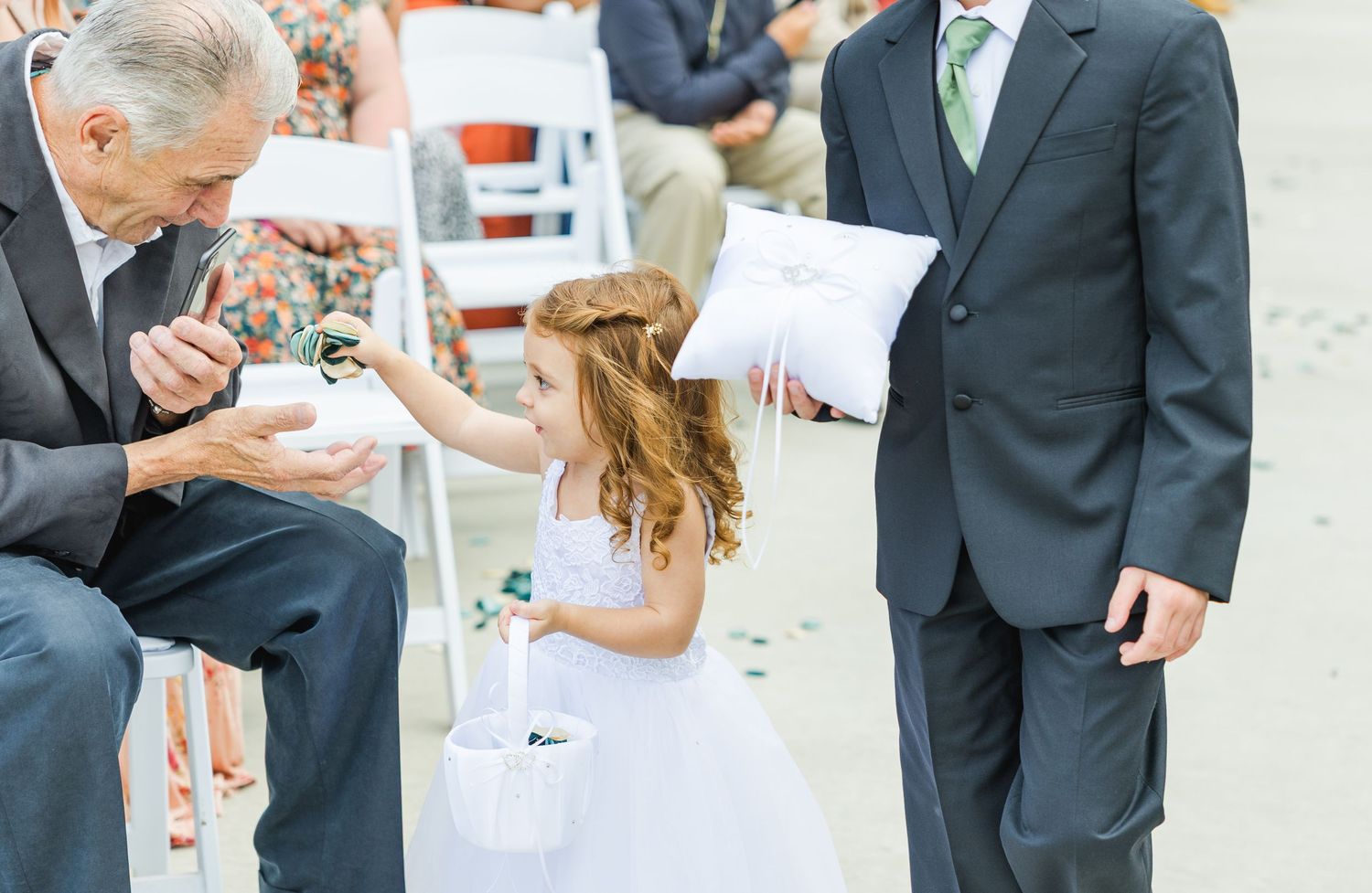 A flower girl in white dress interacting with guests during wedding ceremony.