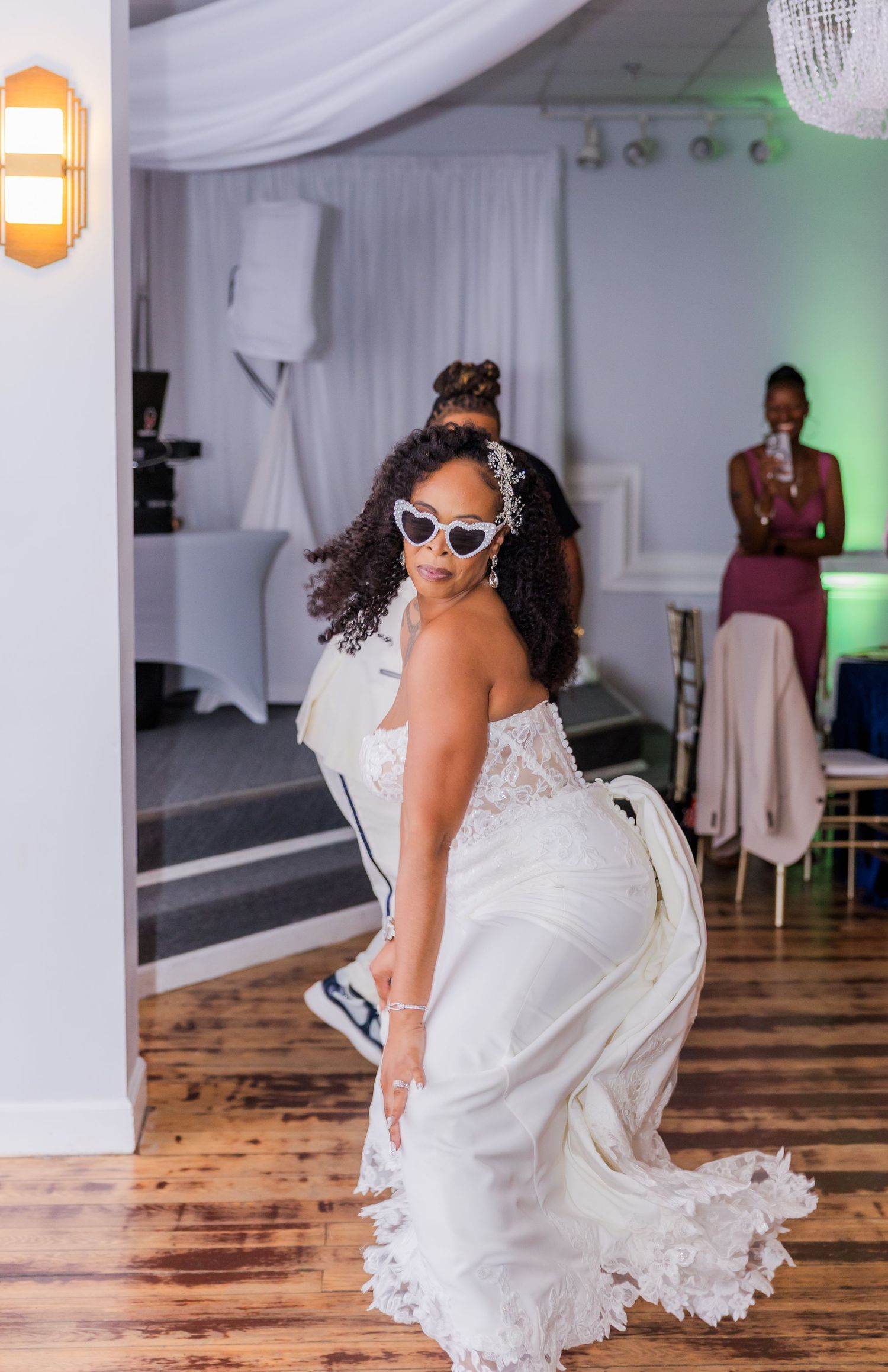 A playful wedding moment captured with retro sunglasses and a white dress against a wooden floor.