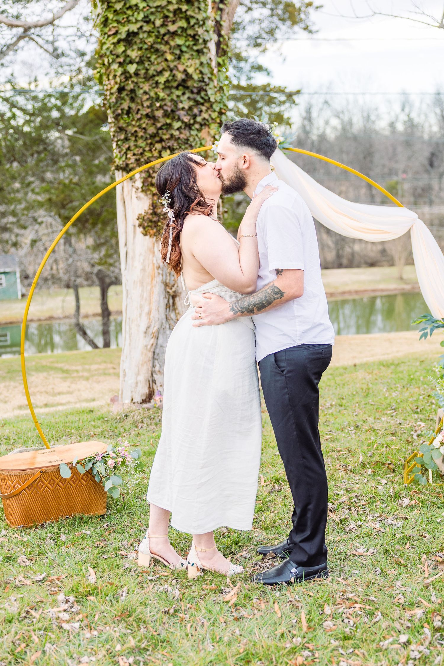 A couple in light spring attire shares a romantic moment outdoors under a tree during a photo session.