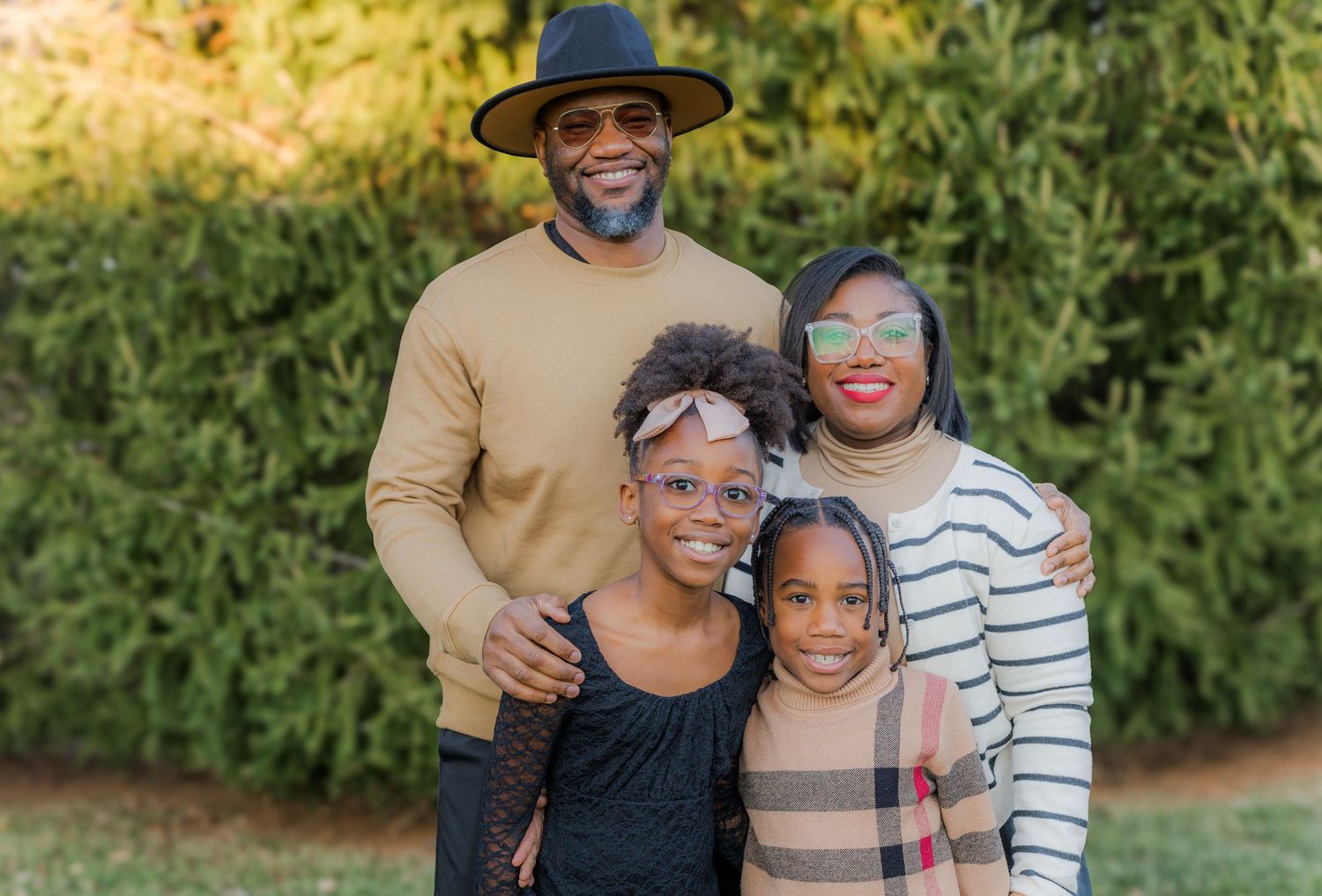Happy family of four posing together outdoors in casual attire.