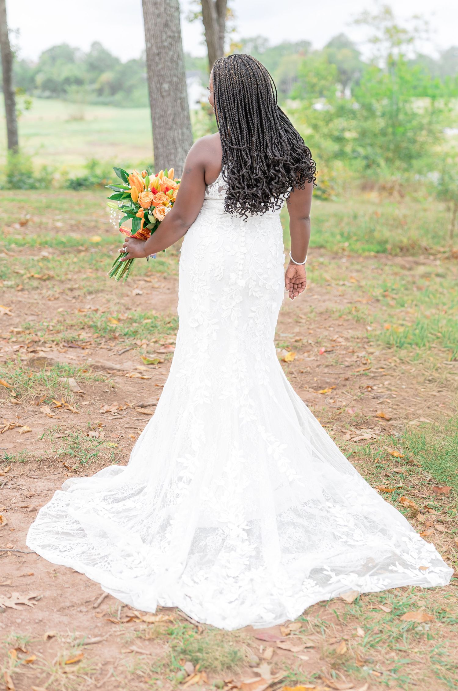 Bride in flowing white lace gown poses in outdoor garden setting.