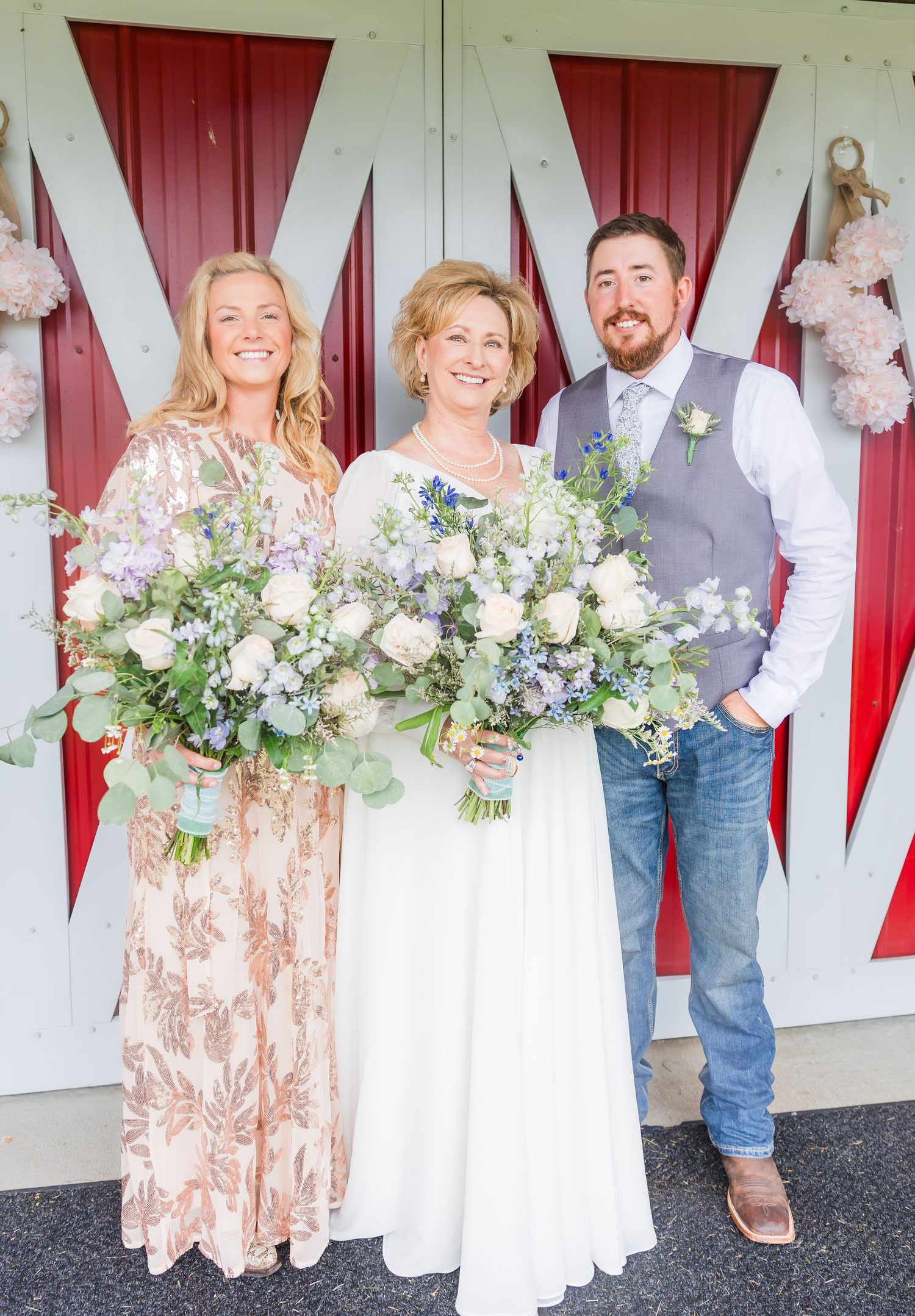 Wedding party poses against white barn doors decorated with elegant floral arrangements.