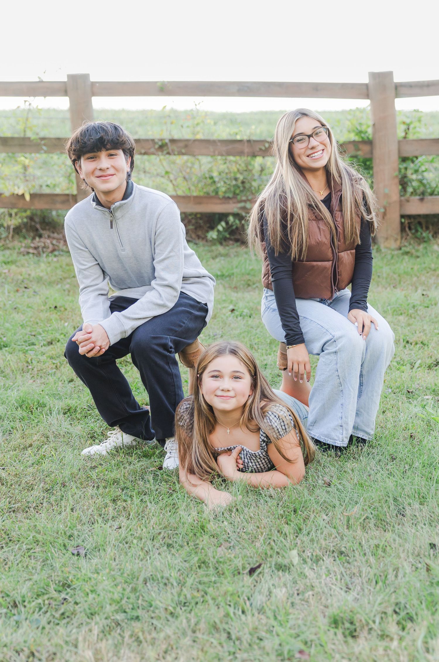 A group of people sitting casually on grass near a wooden fence in casual attire.