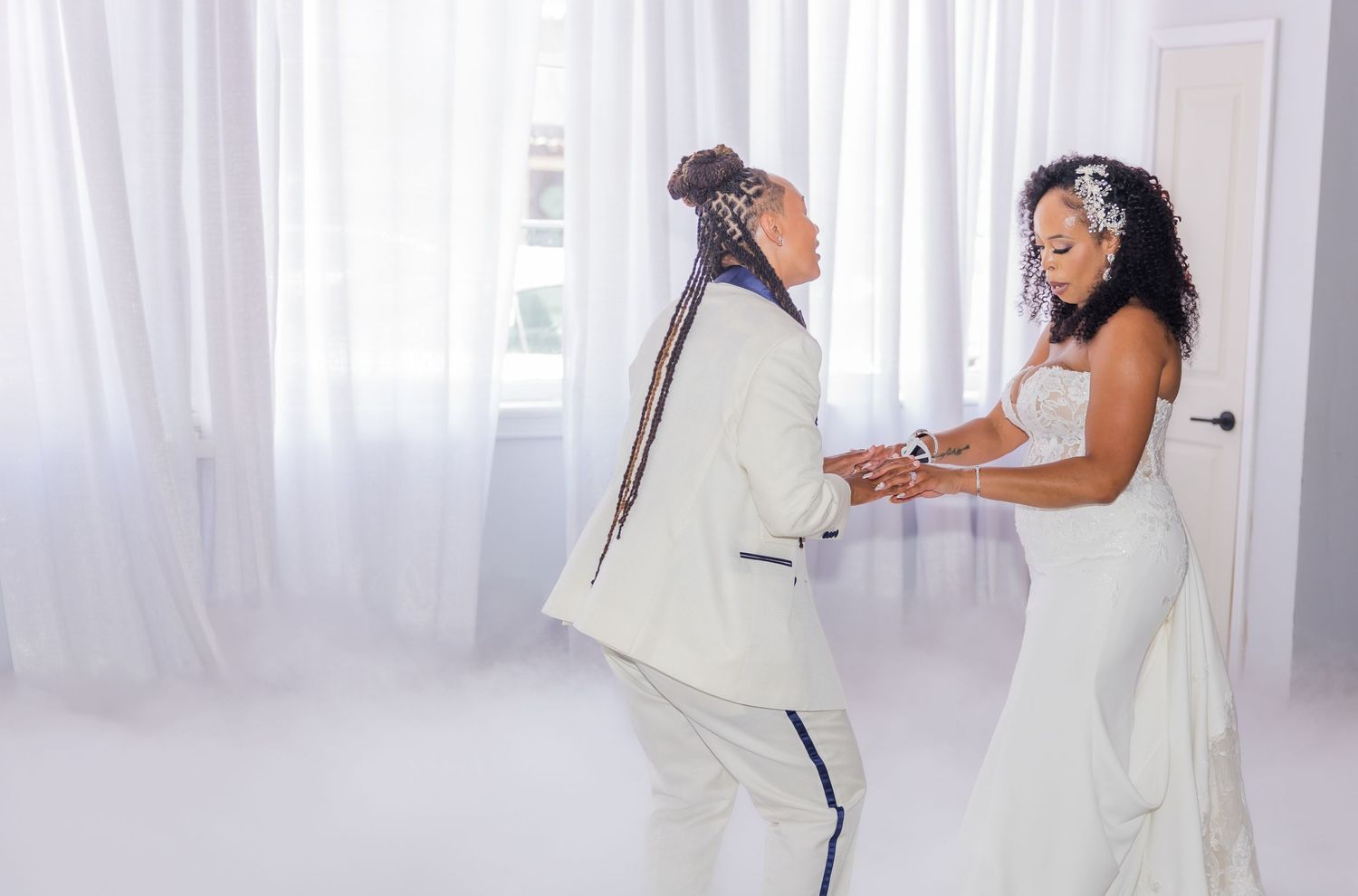 A joyful wedding dance moment captured in a bright white room with flowing curtains.