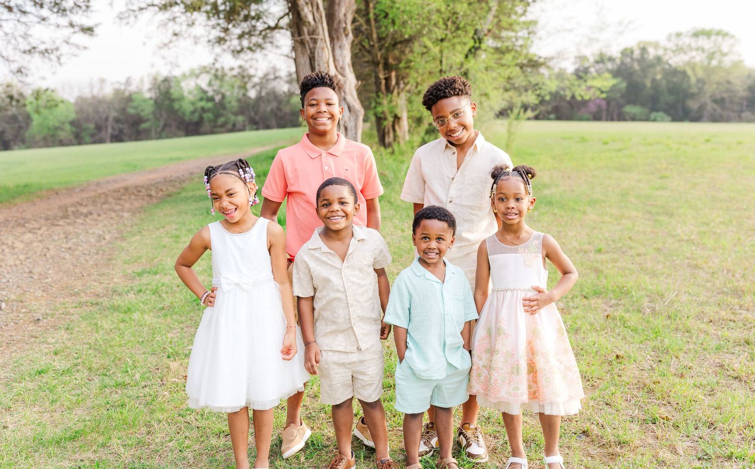A family group poses together outdoors wearing coordinated pastel and white outfits.