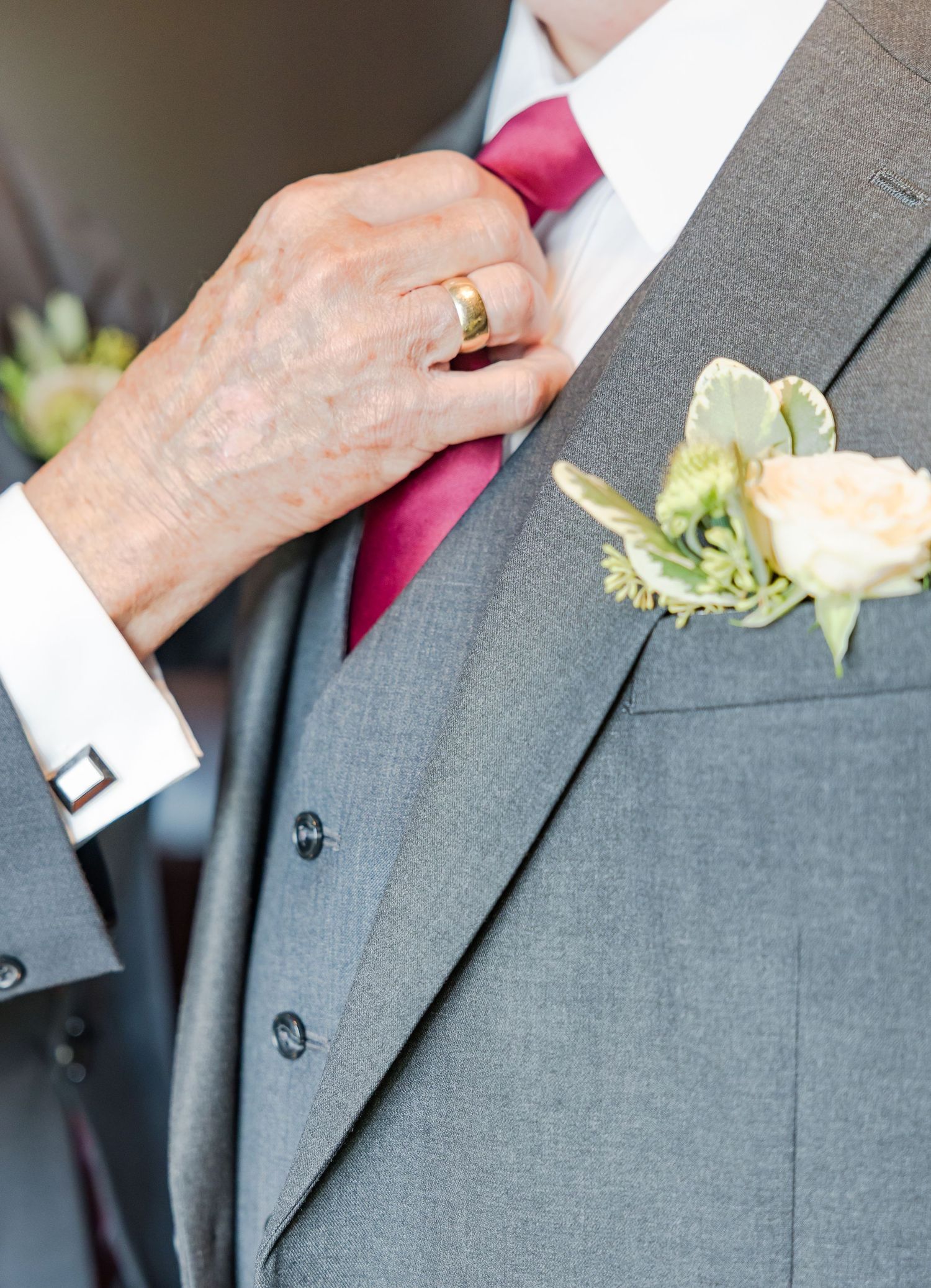Detail shot of a boutonniere with white roses on a gray suit lapel with red tie.