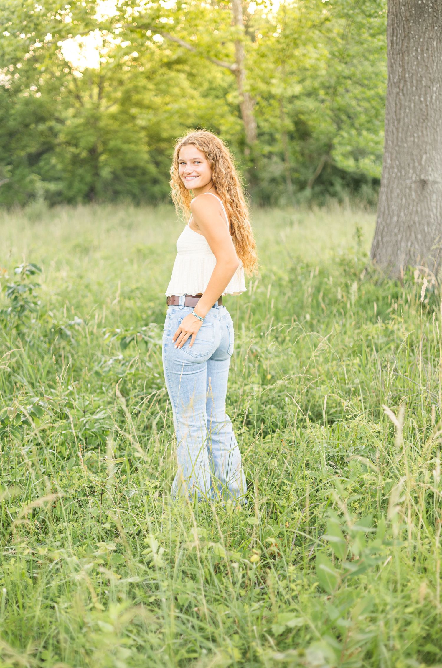 A casual summer portrait in jeans and white top standing in a sunlit meadow.