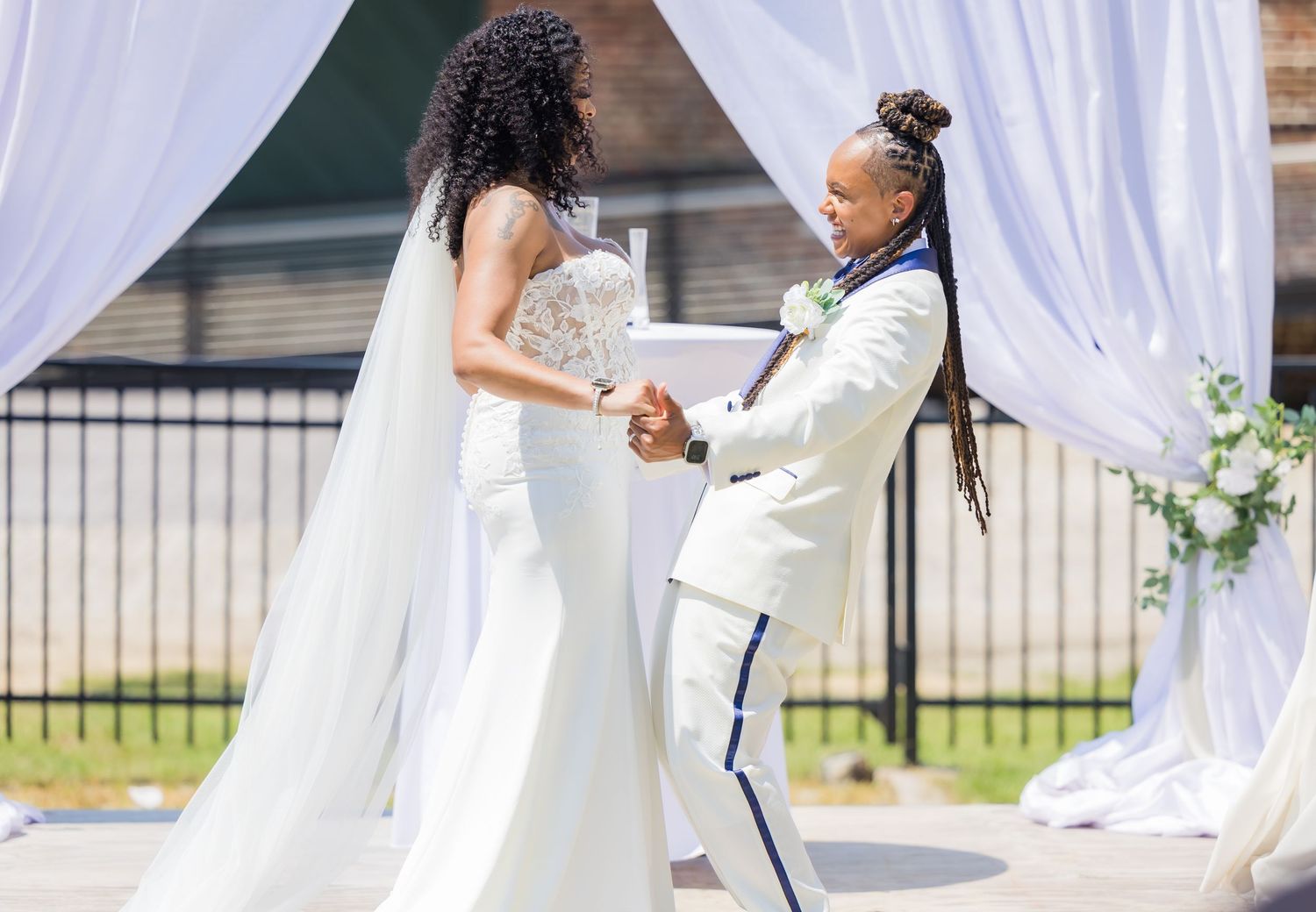 Wedding ceremony under white drapes with couple exchanging vows.