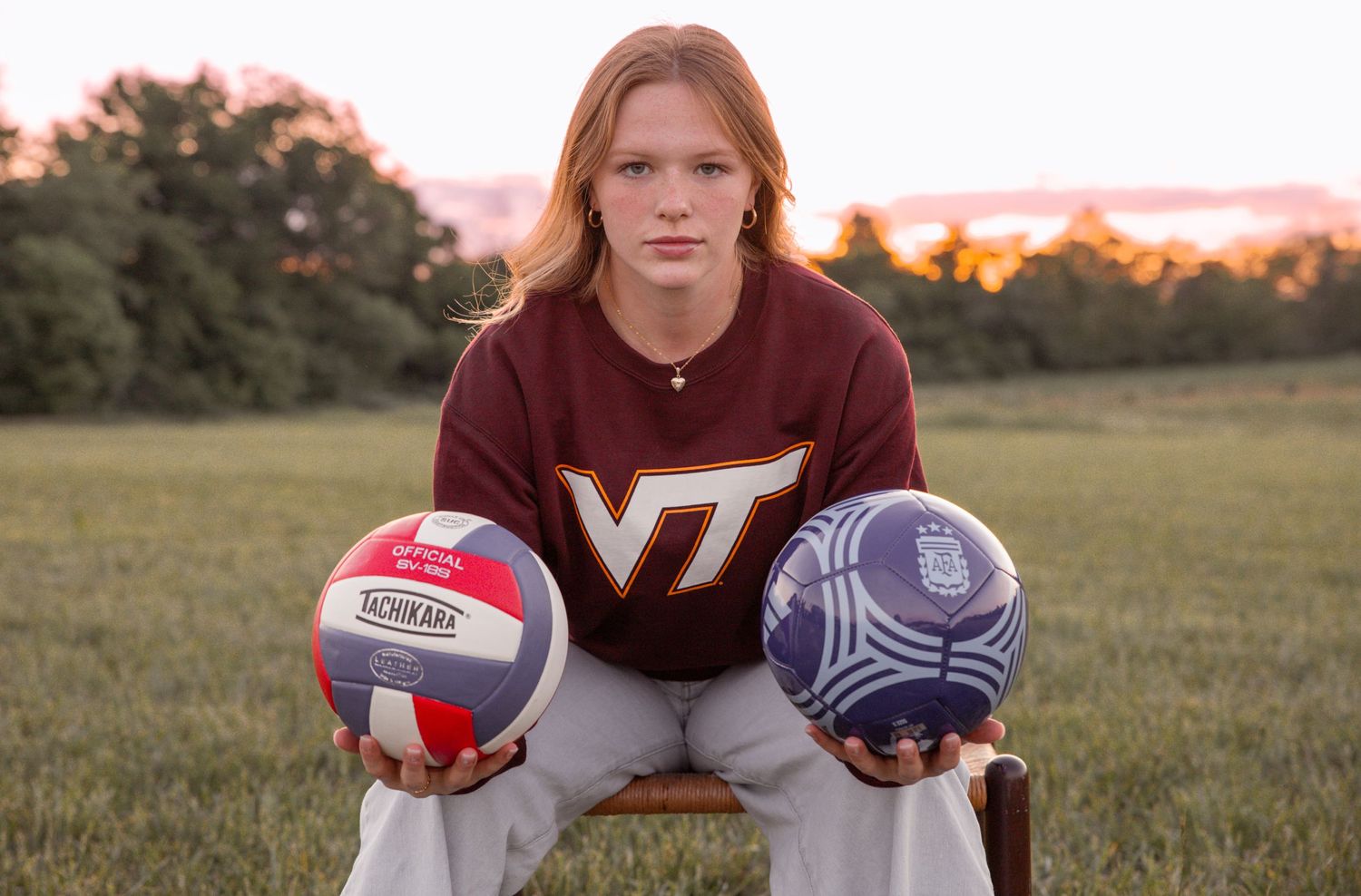 Virginia Tech student athlete posing with volleyball and soccer ball at sunset.