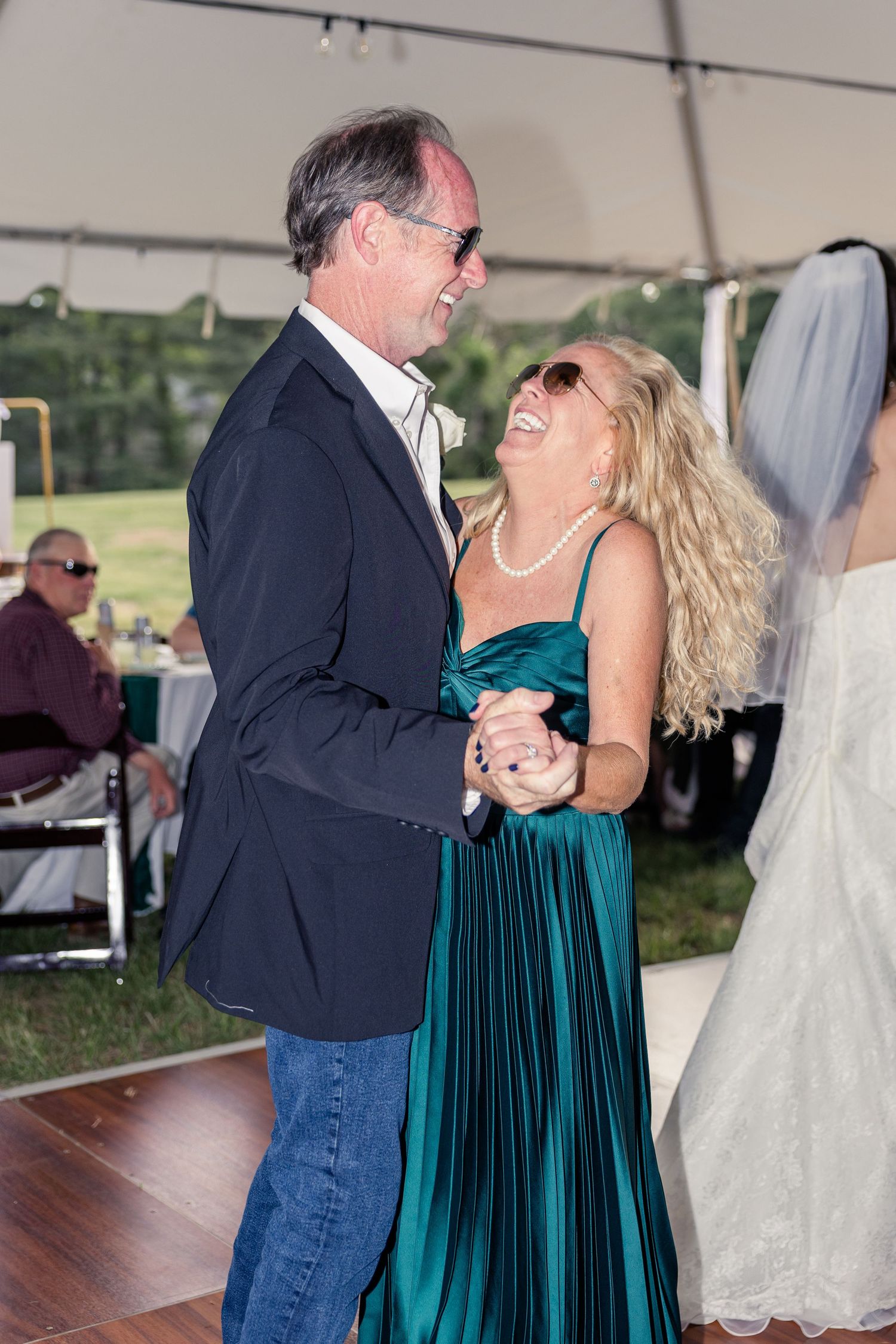 Couple laughing and dancing together at an outdoor wedding reception under a white tent.