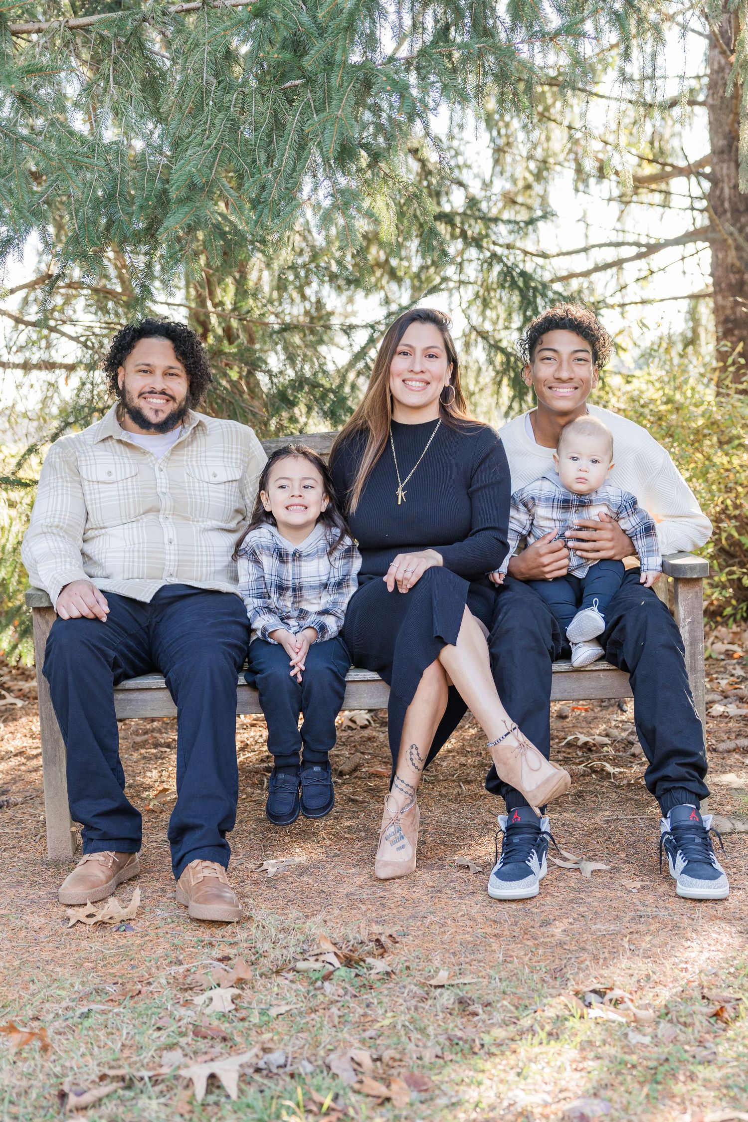 Family sitting together on ground in forest wearing coordinated blue and white outfits for outdoor photo session.
