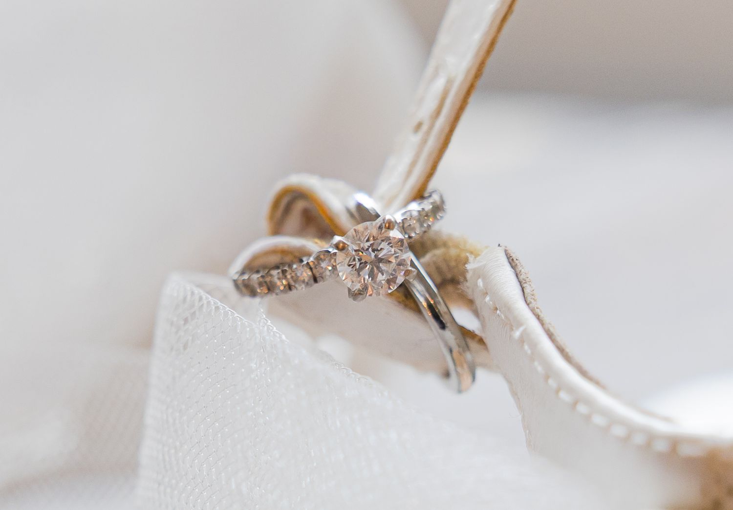 Close-up of a delicate diamond wedding ring on white fabric.