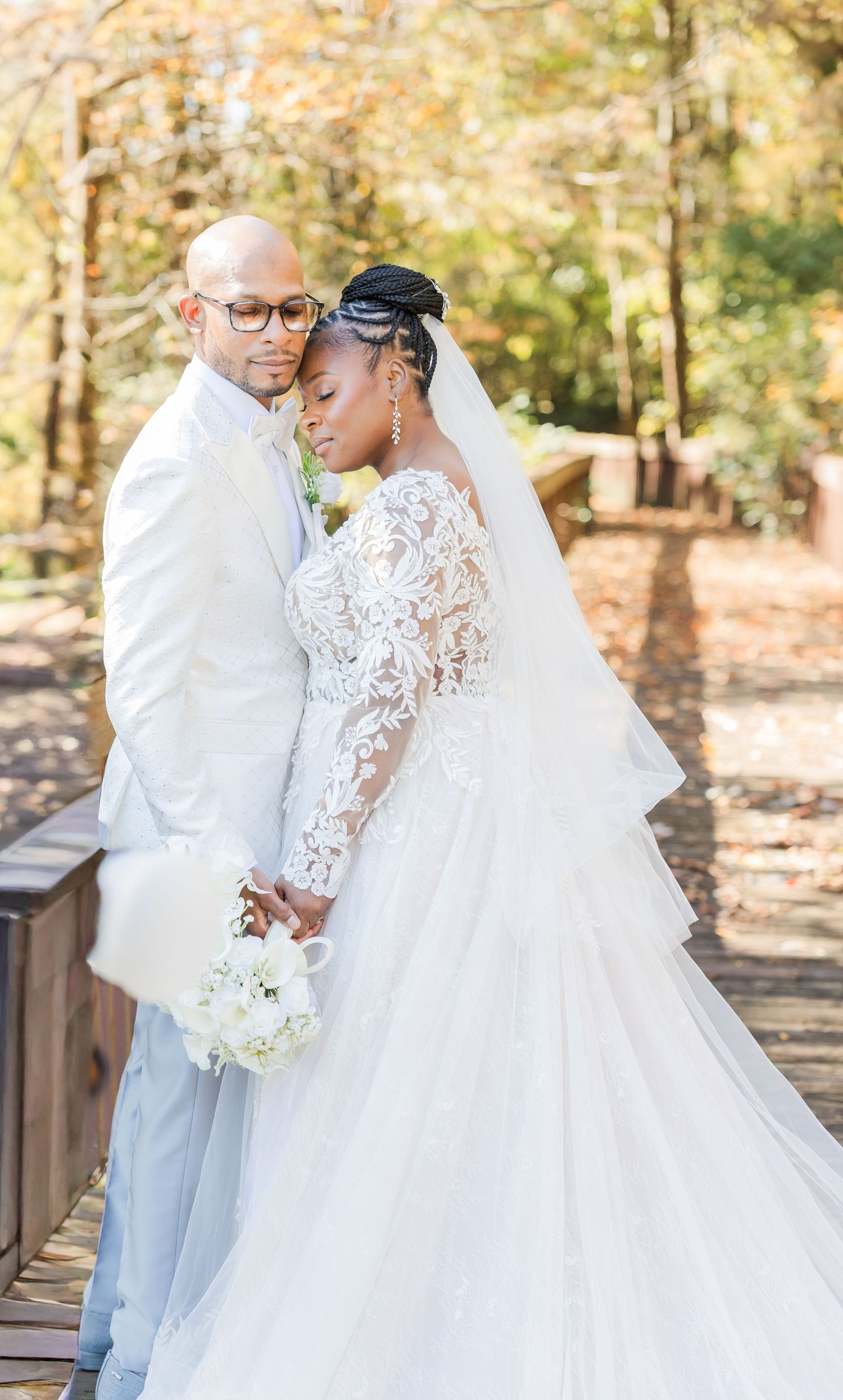 A romantic wedding couple embraces on a rustic wooden bridge surrounded by autumn foliage.