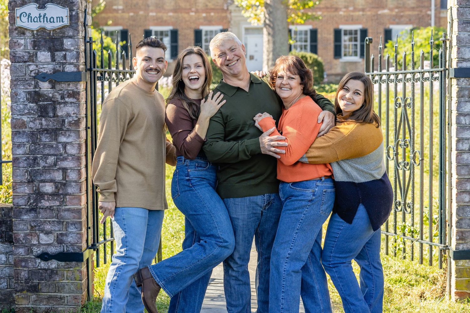 A group poses playfully together against an iron gate and brick wall backdrop.