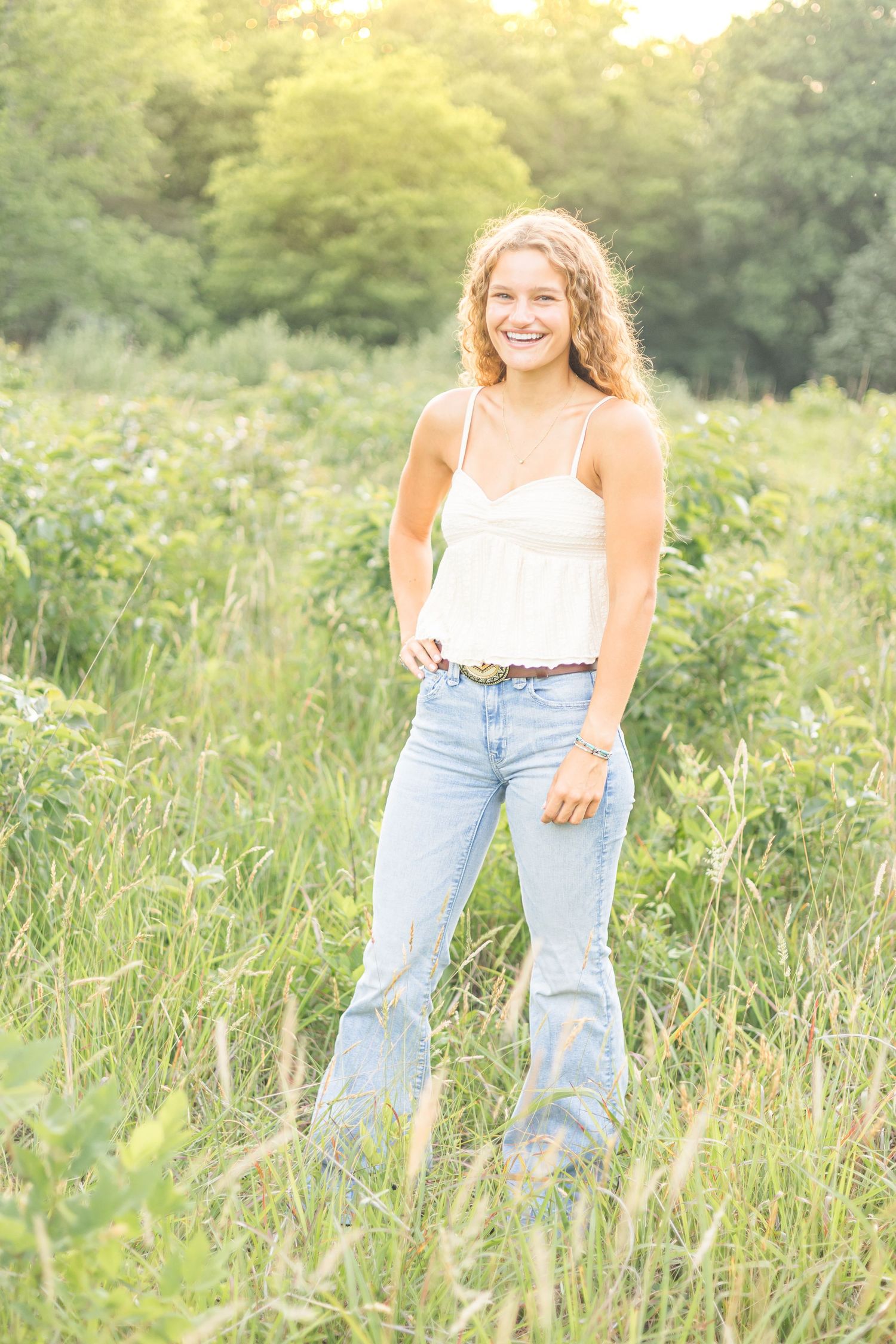 A casual summer portrait in light wash jeans and white tank top in a sunlit field.