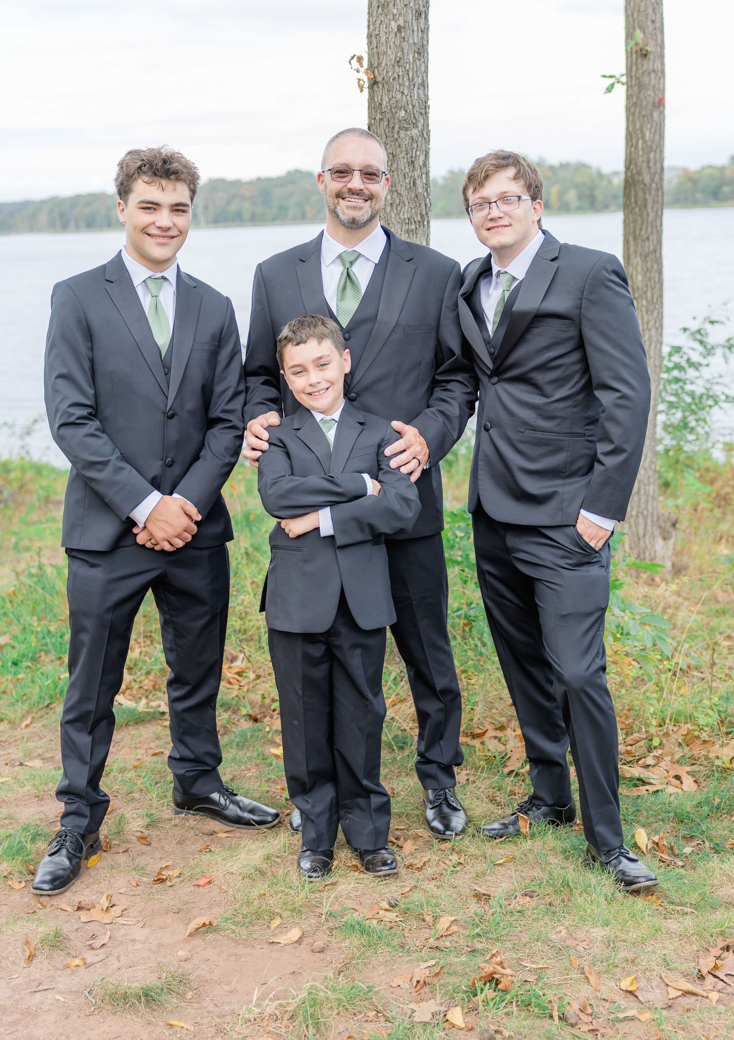 Groomsmen in dark suits strike playful poses during outdoor wedding photo session.