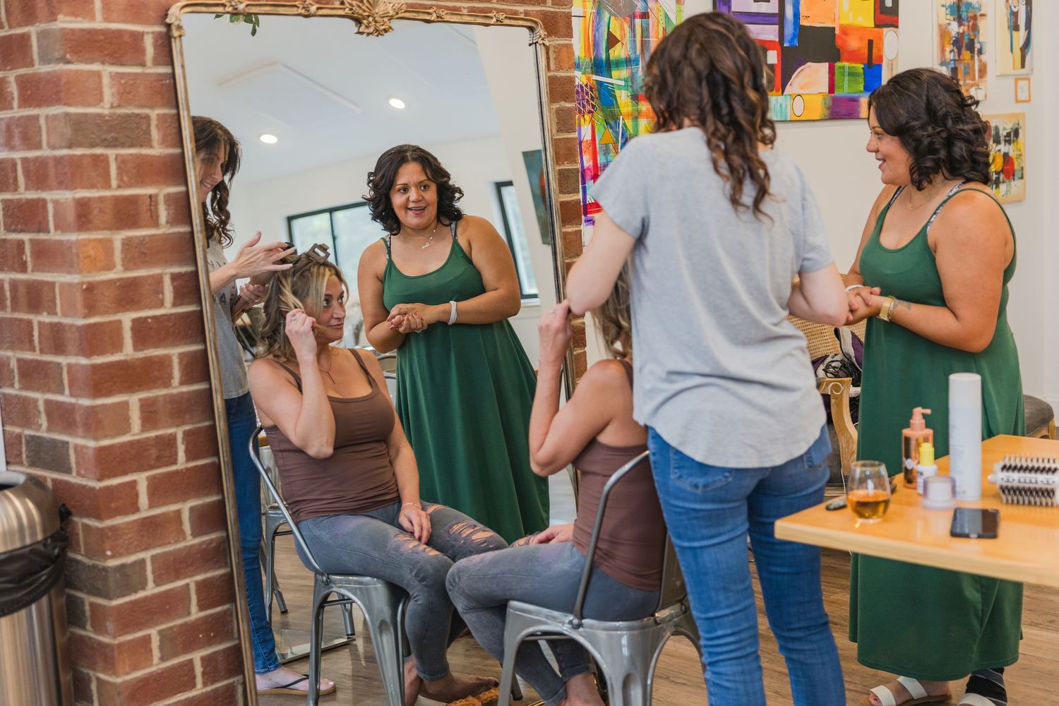 Beauty salon scene with stylists and clients reflected in an ornate mirror against brick wall.