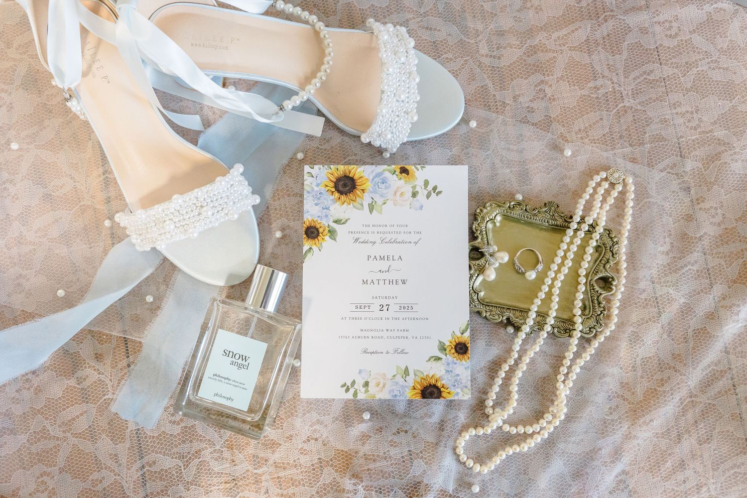Wedding accessories including white shoes, sunflower invitation, and pearl necklace on textured surface.