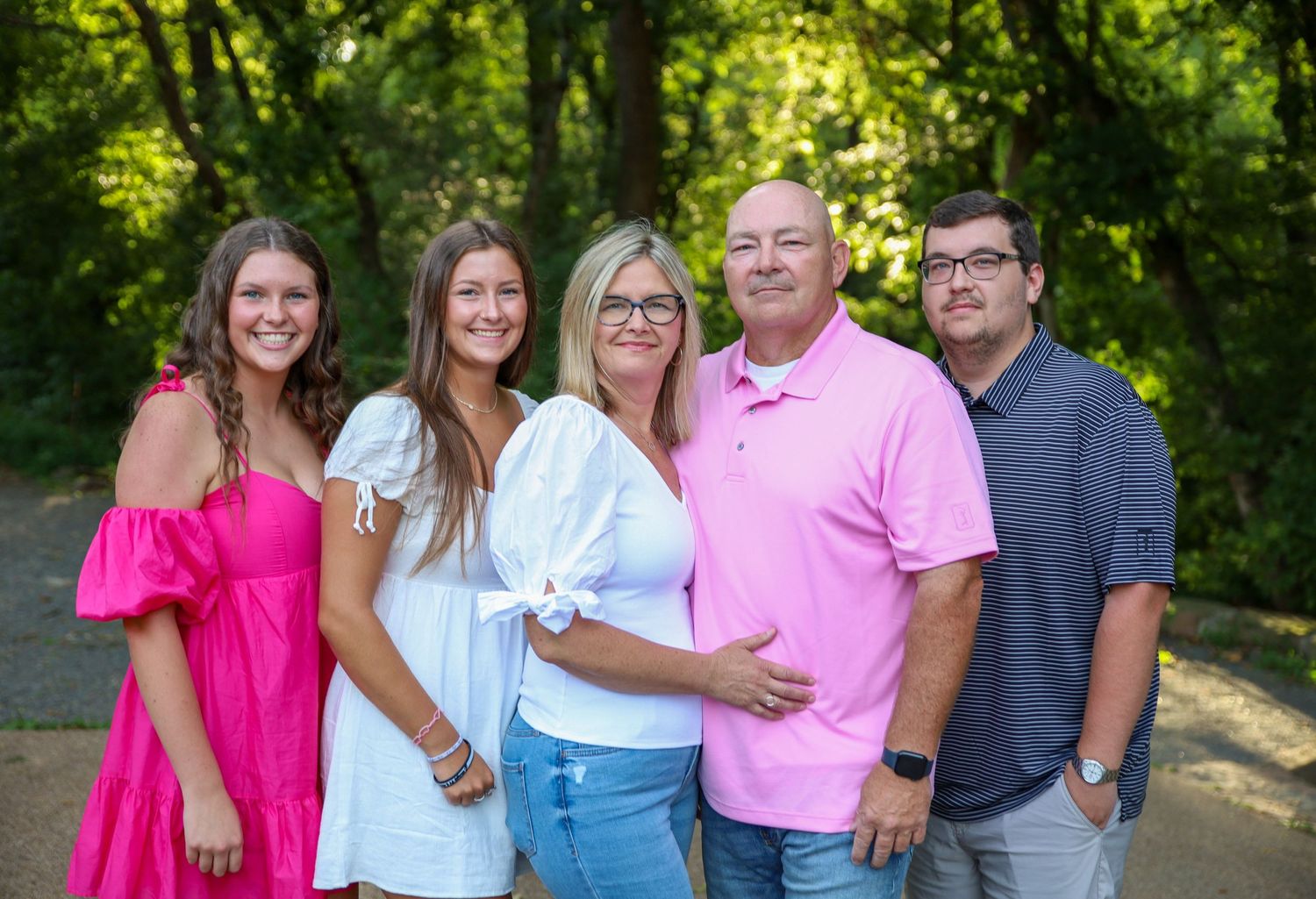 Group photo of people in coordinated pink and white outfits standing together in a wooded setting.