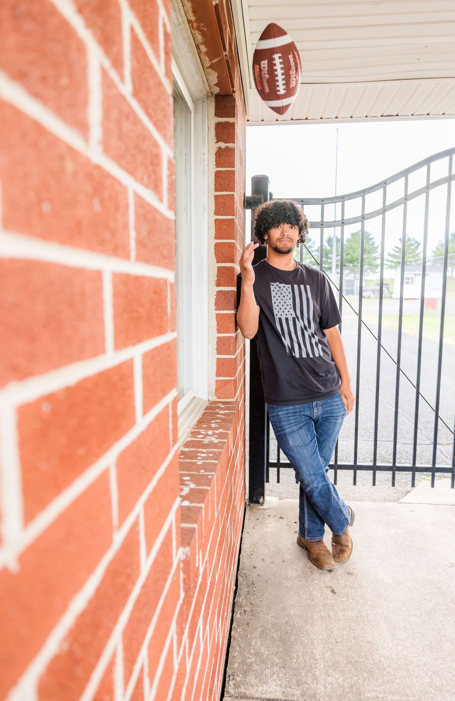 Person in casual wear leans against brick wall near football decor.