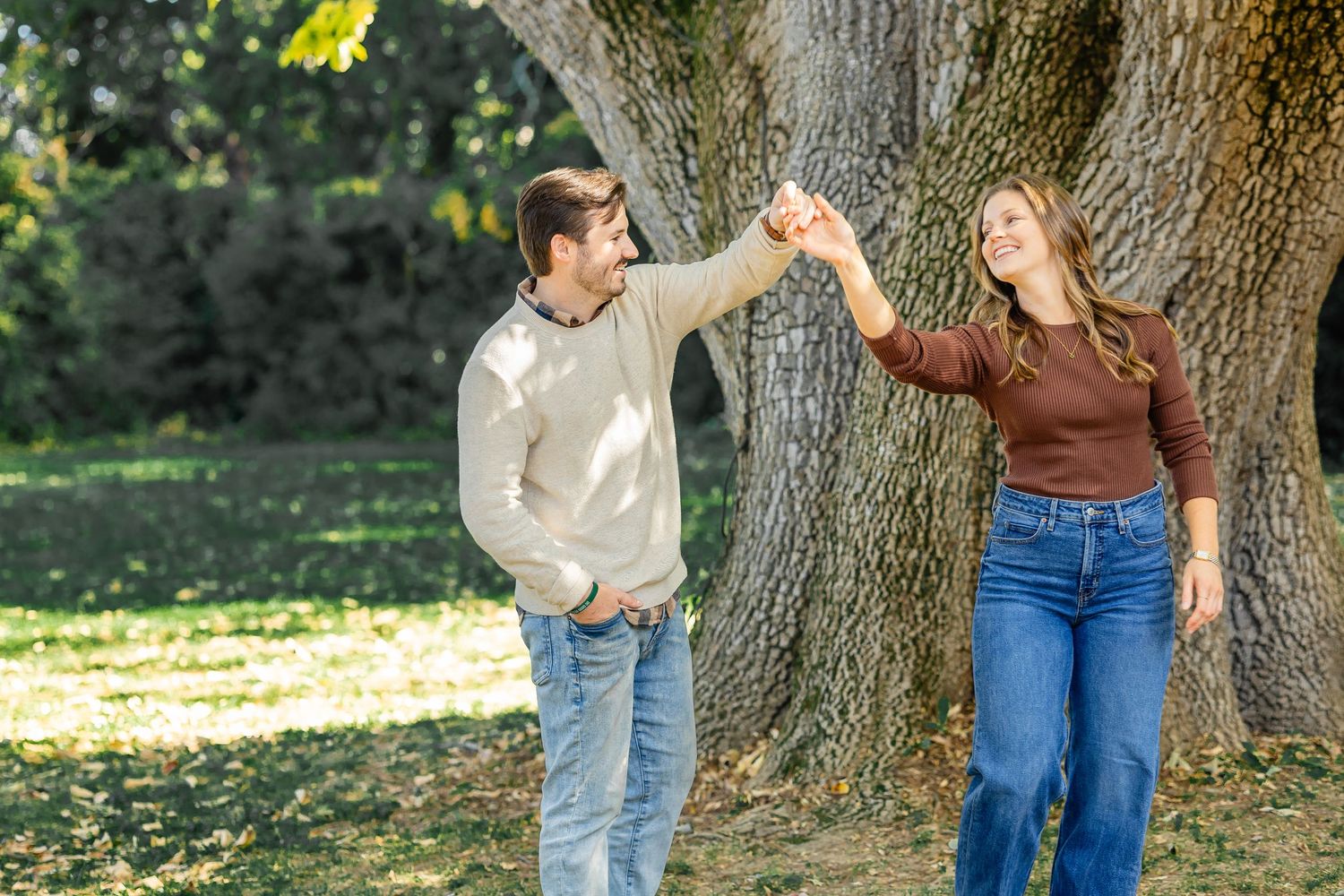 Couple dancing and twirling near large tree in outdoor setting.