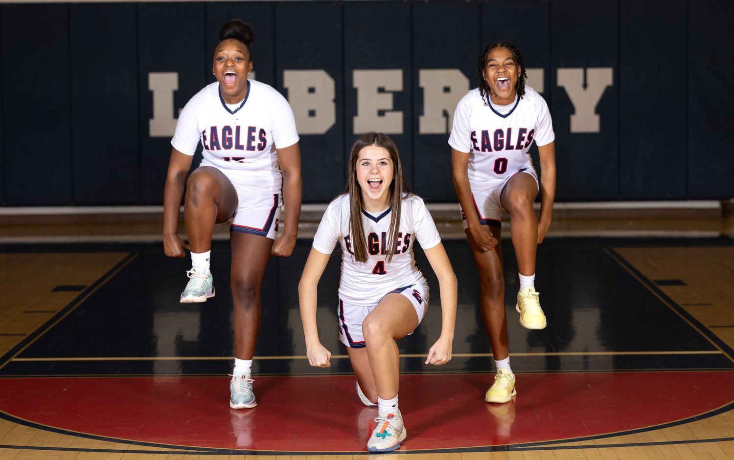 Basketball team members pose in white Eagles uniforms on red court.