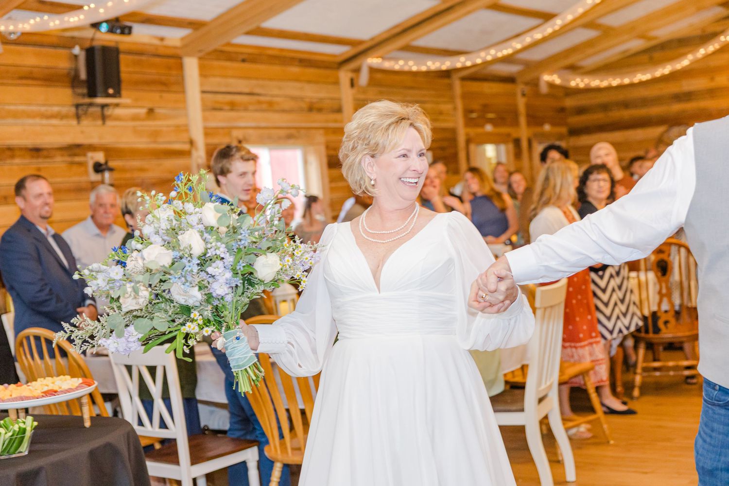 Couples dancing together in a rustic wooden barn reception hall with warm lighting and elegant decor.