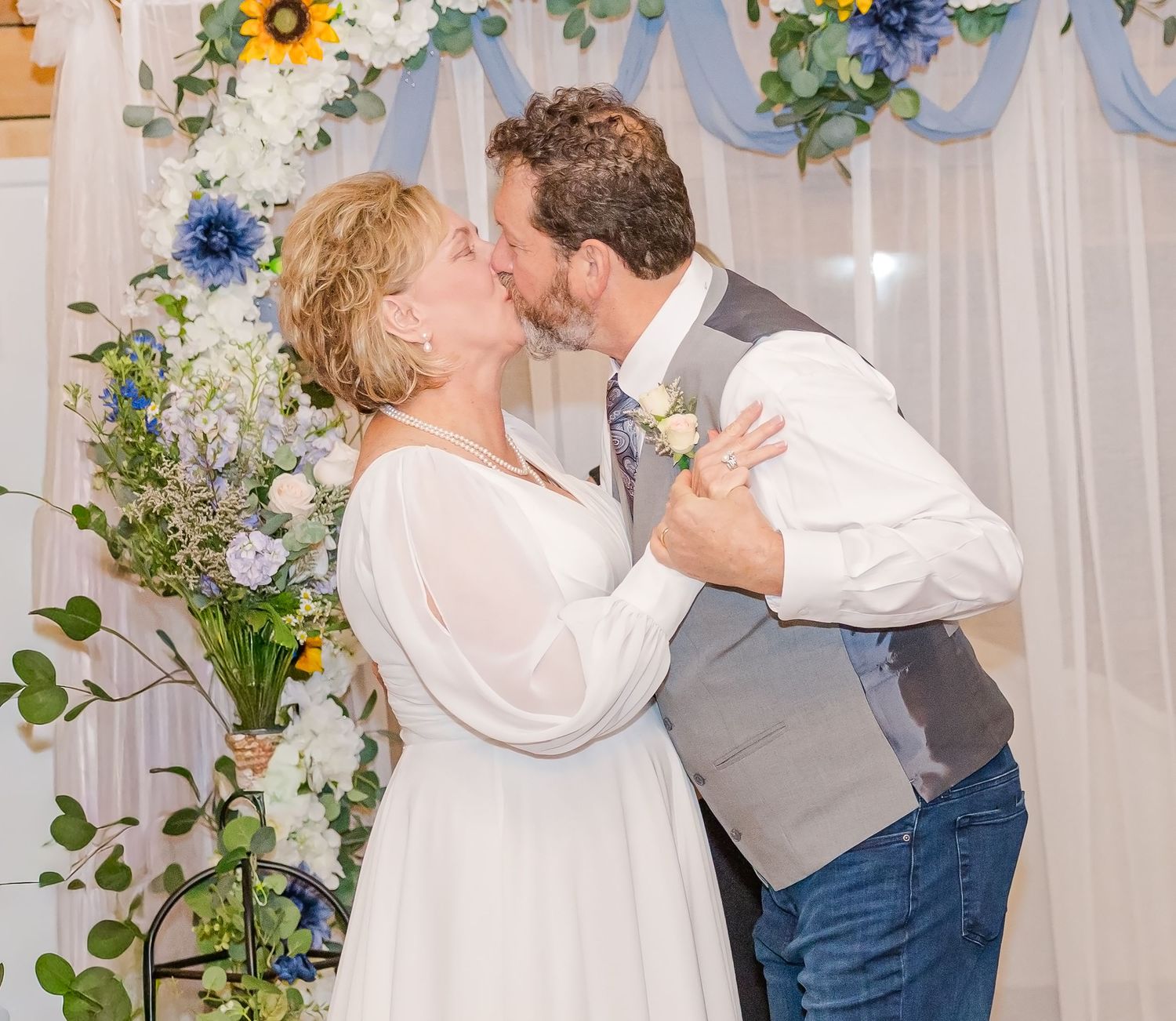 Wedding couple sharing their first dance under floral decorations and white drapery.