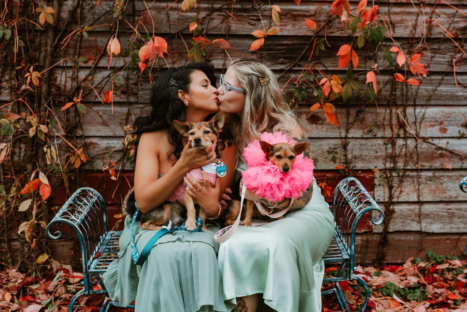A romantic couple in mint green outfits poses together against a rustic wooden wall with autumn foliage.