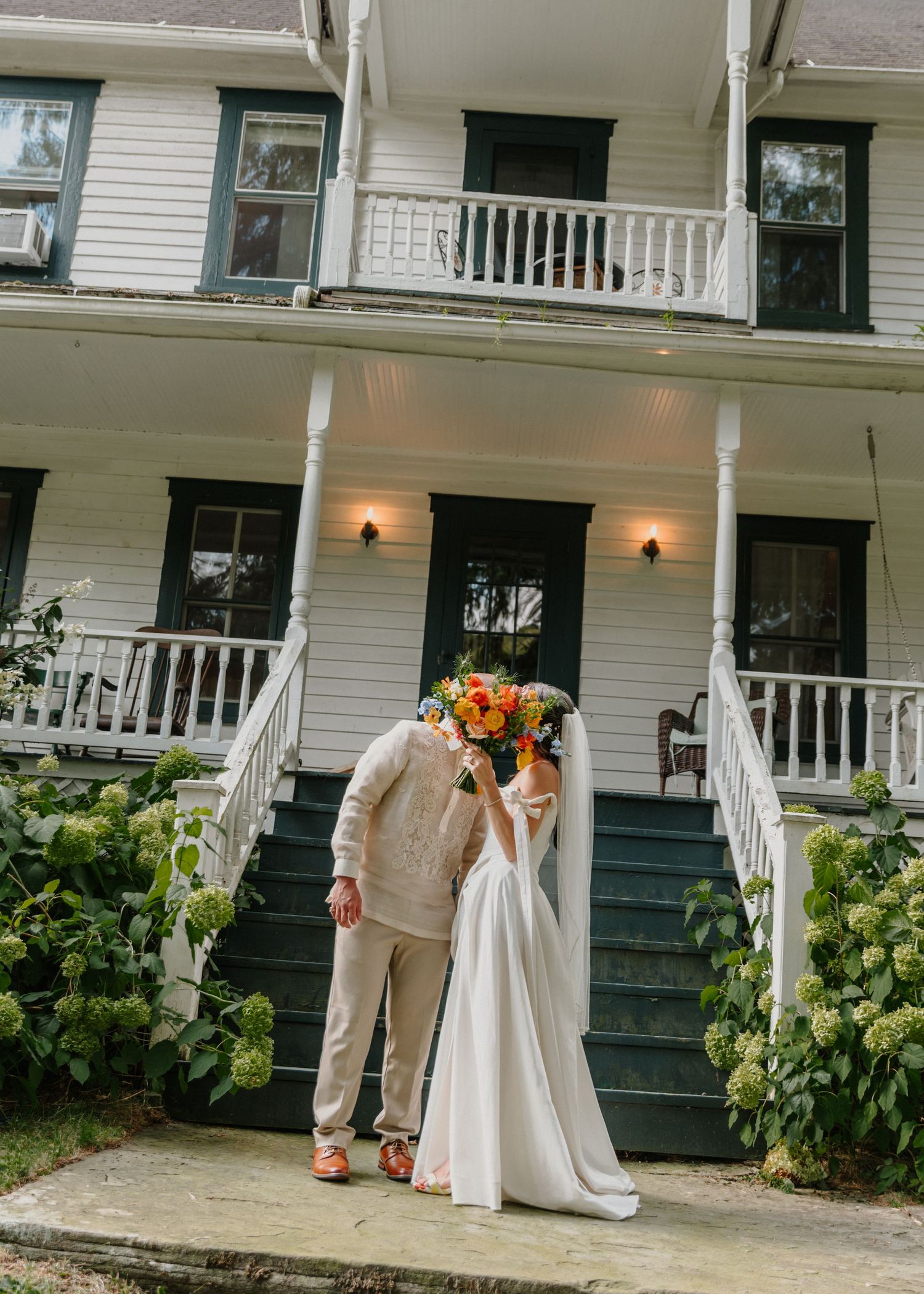Wedding party stands on a white porch of a classic house with elegant columns and black shutters.