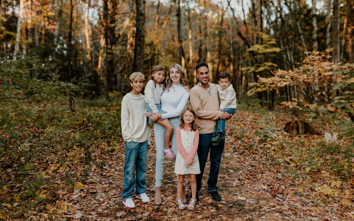 A family walks together through a vibrant autumn forest with fallen leaves scattered along the path.