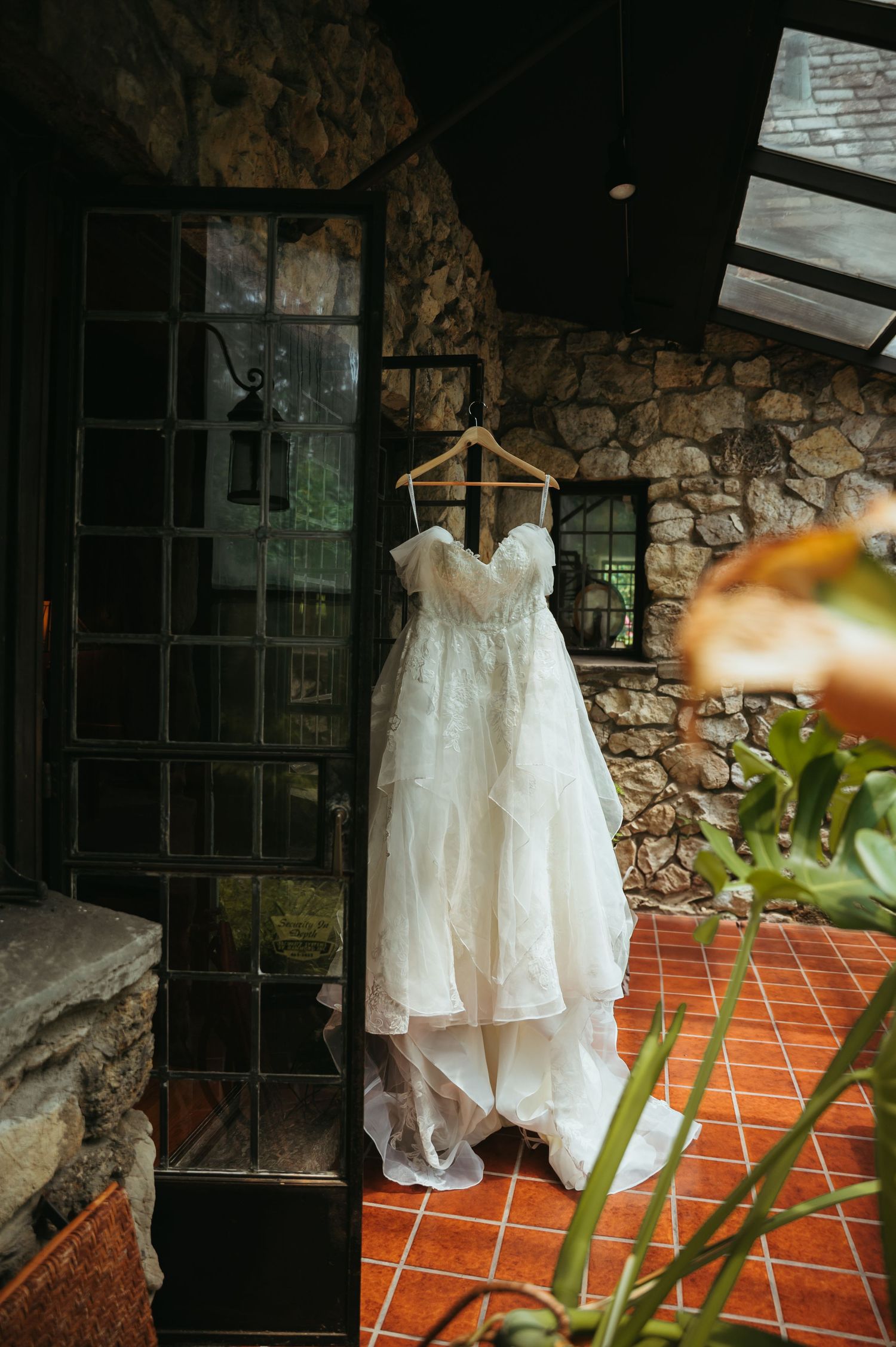 White lace wedding dresses hanging on hangers against a rustic stone wall with terracotta tiles and natural lighting.