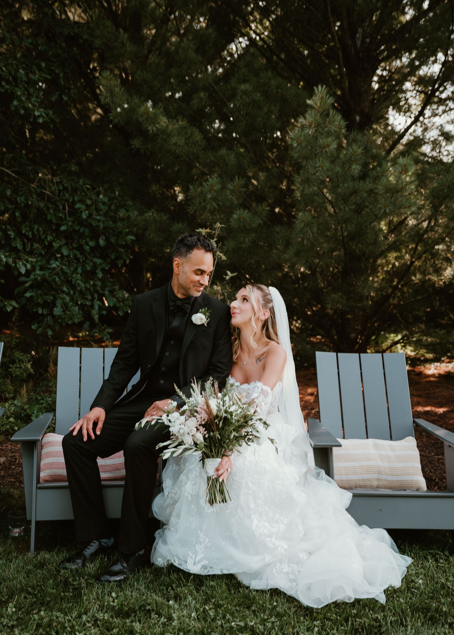A couple sits together on an Adirondack chair during sunset in a garden setting.
