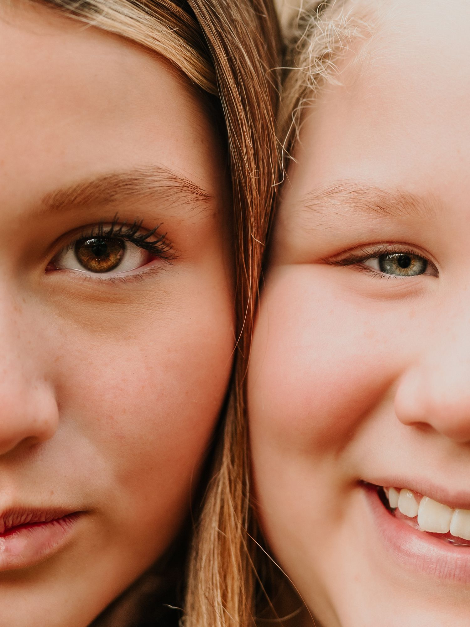 Close-up portrait composition showing warm smiles and brown hair against neutral background.