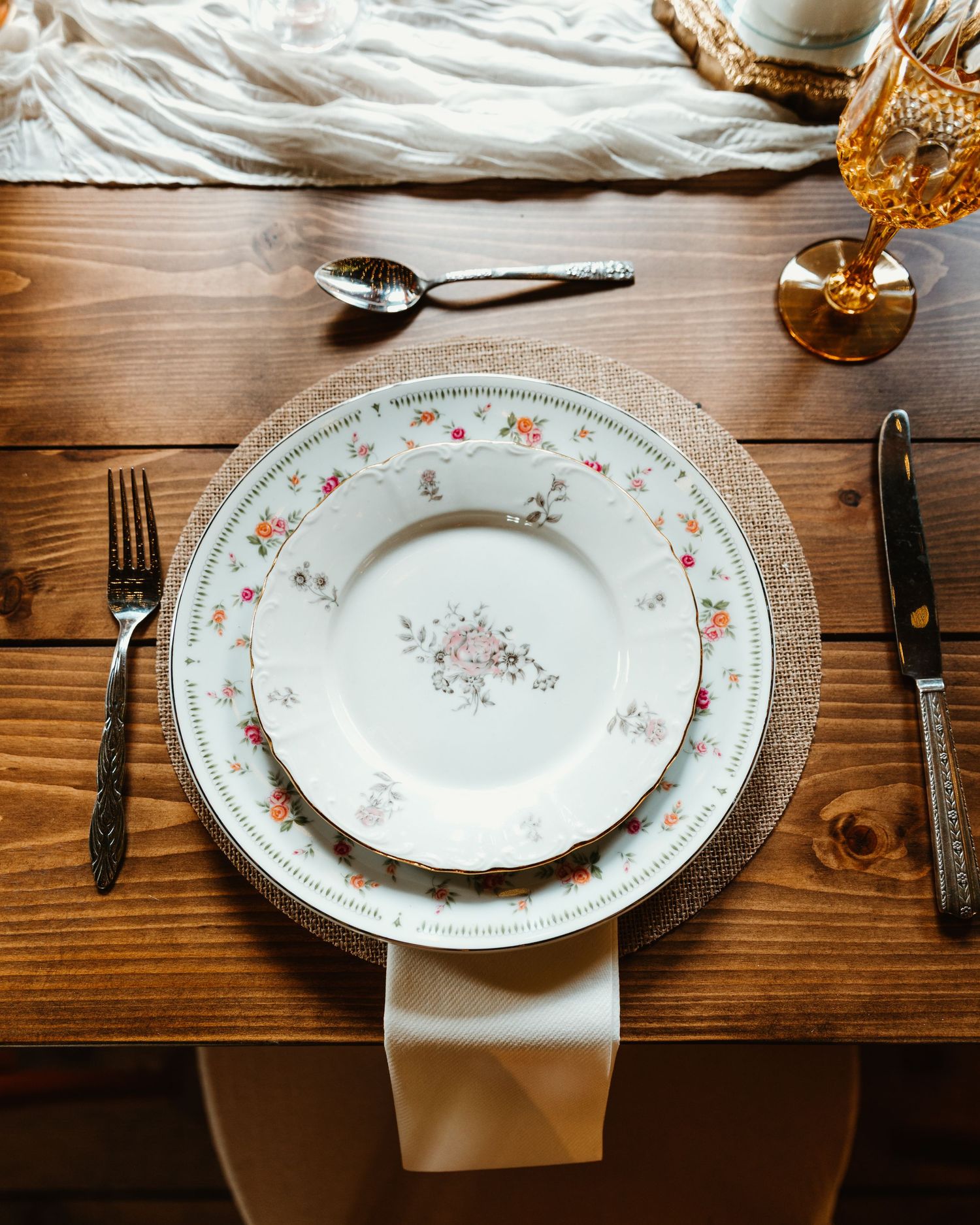 Place settings with elegant white plates and gold accents on a rustic wooden table for a formal dining event.