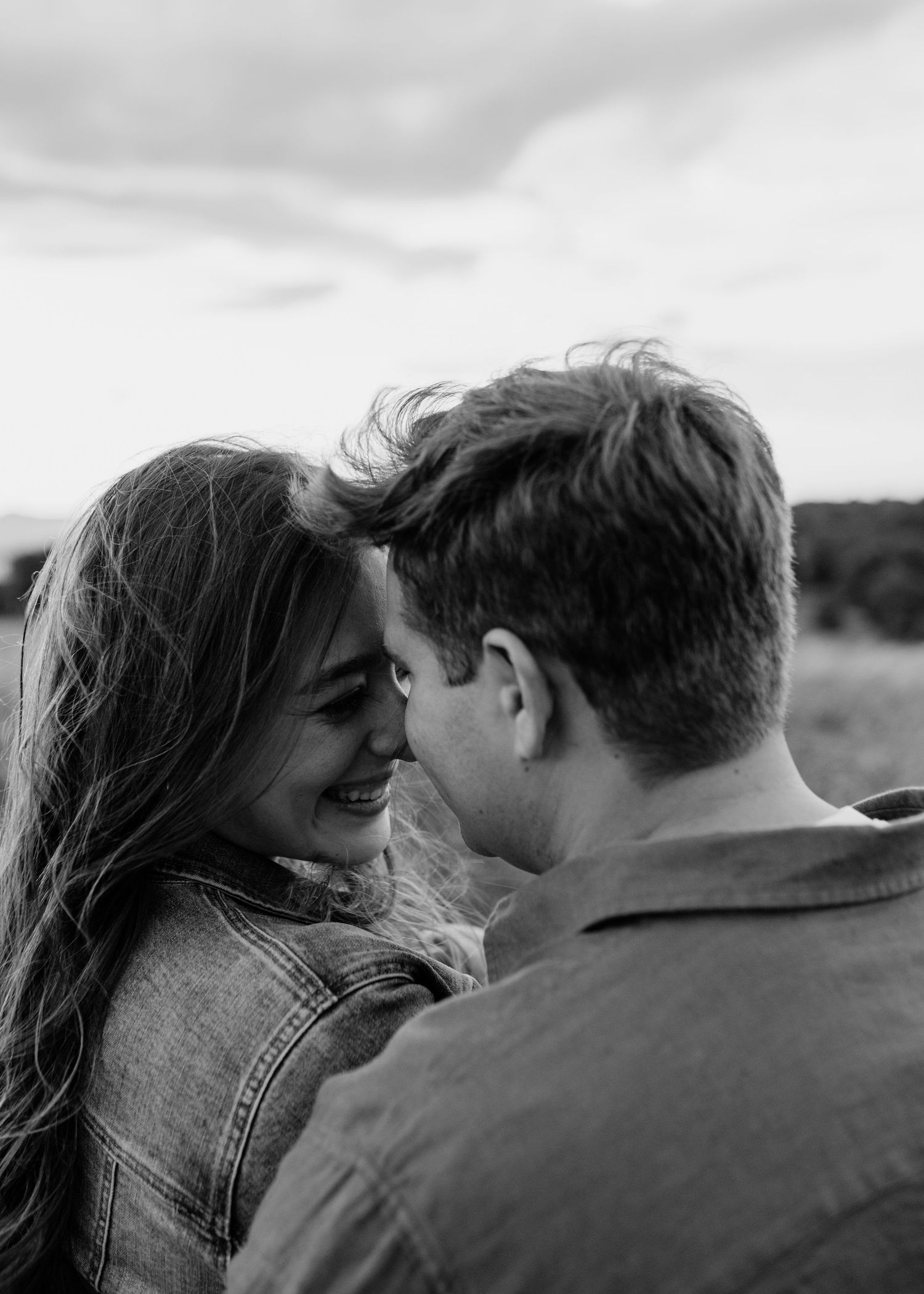 Black and white photo of a smiling couple sharing a romantic moment outdoors in a field.