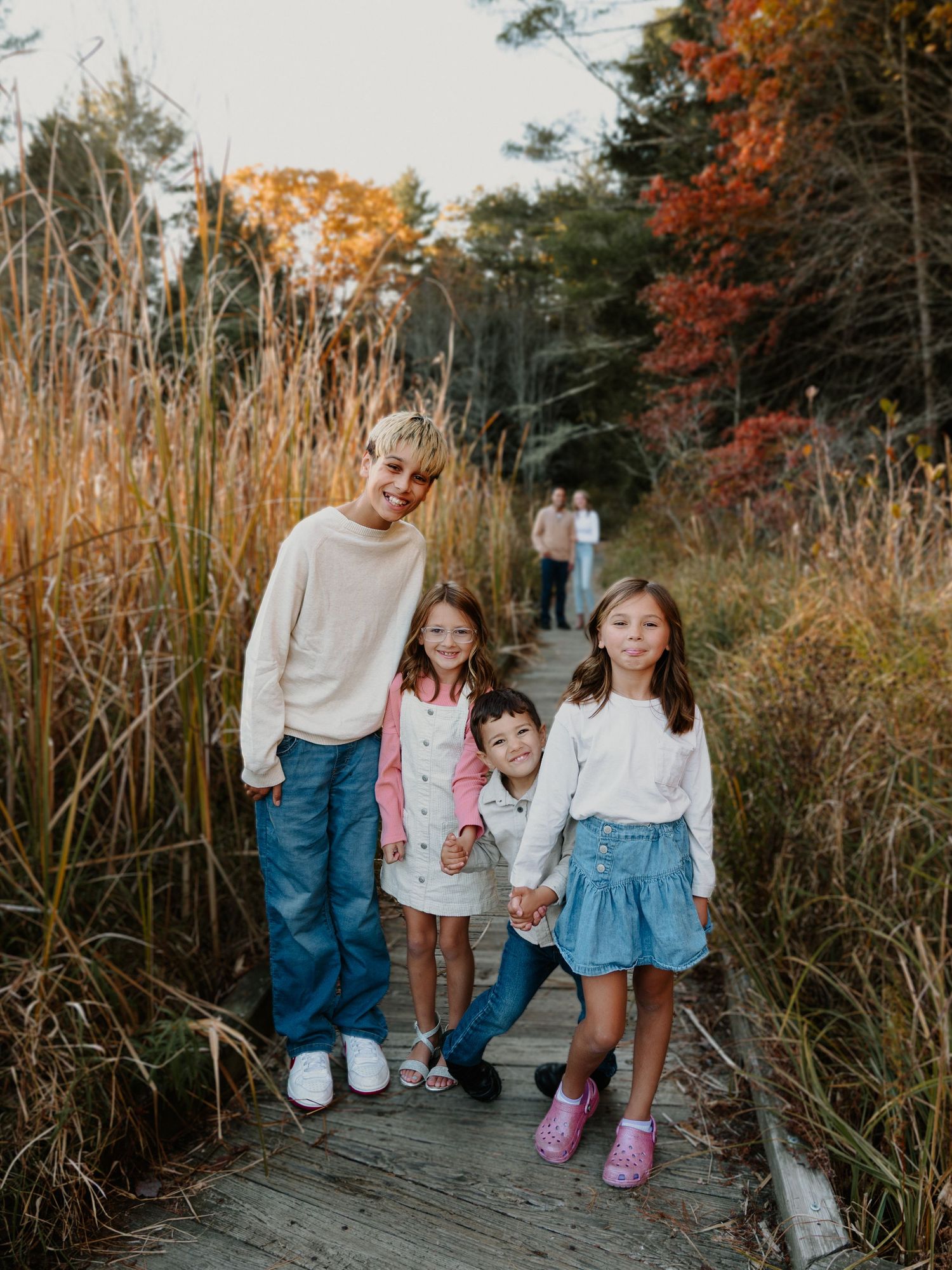 Family enjoying autumn scenery together on a nature path surrounded by tall grass and fall foliage.