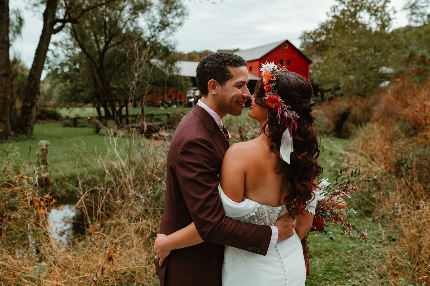 A couple shares romantic moments in a rustic outdoor setting with red barns and autumn foliage in the background.