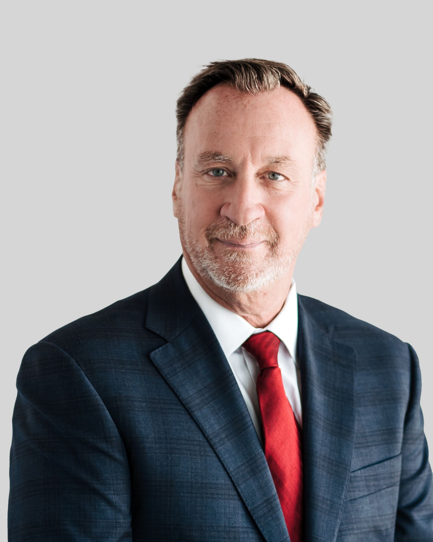 Executive portraits featuring a navy suit and red tie against a light background.