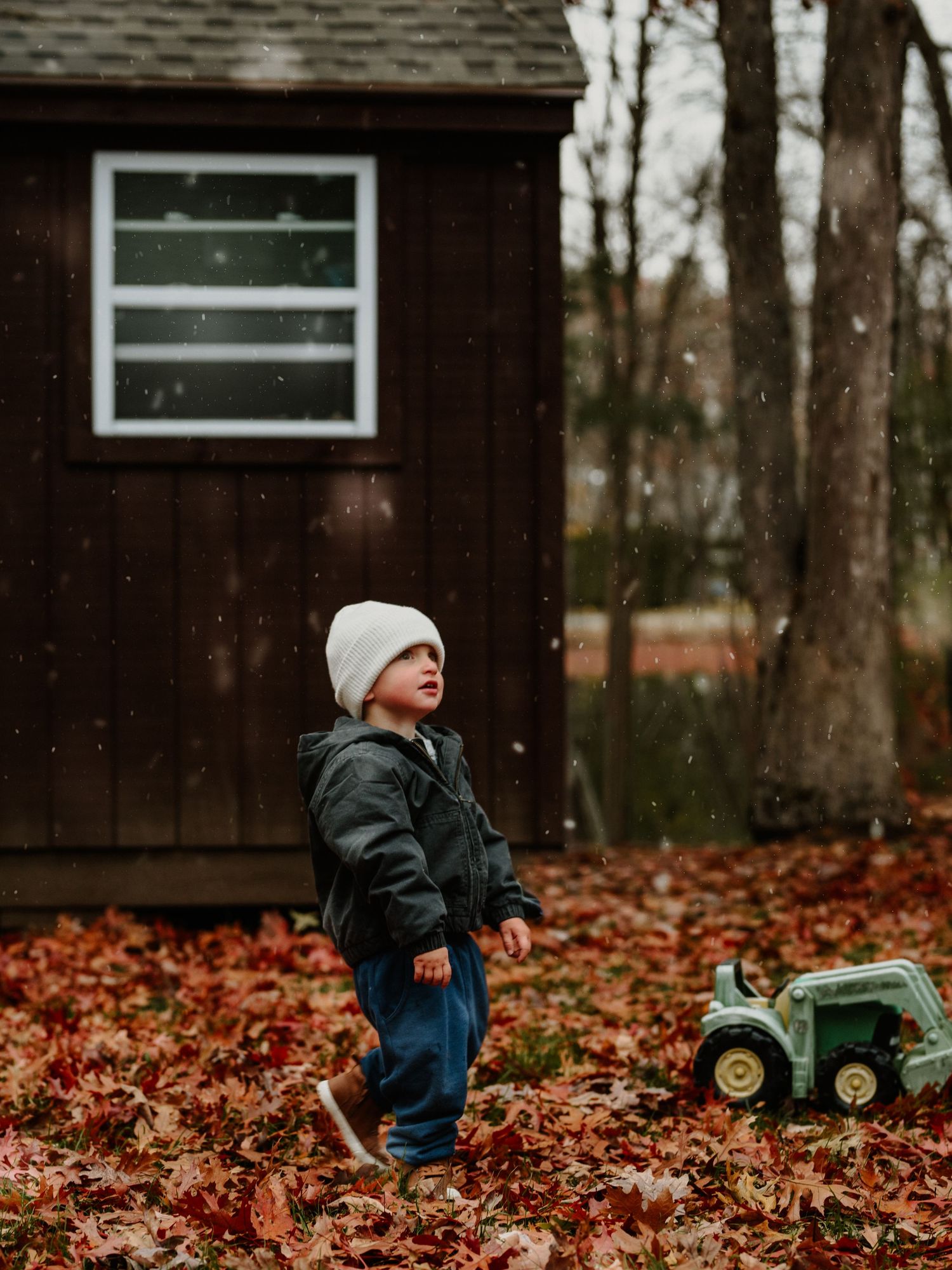 Child plays with toy tractor in fallen autumn leaves on a moody overcast day.
