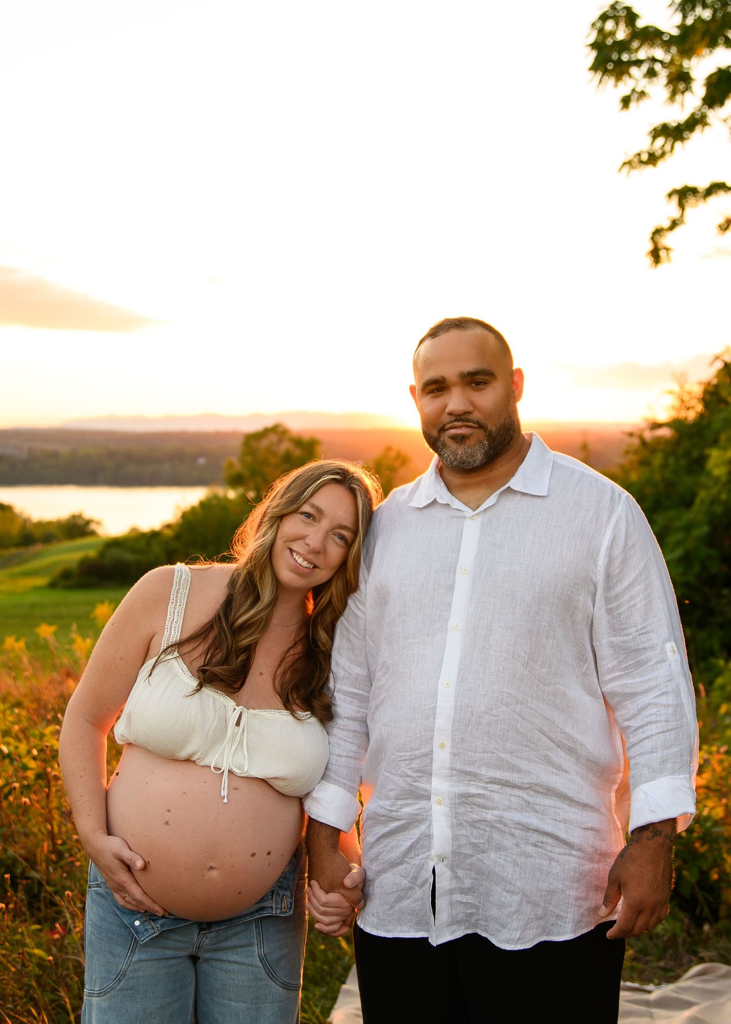 Maternity photo series of a couple in white outfits posing outdoors during golden hour sunset.