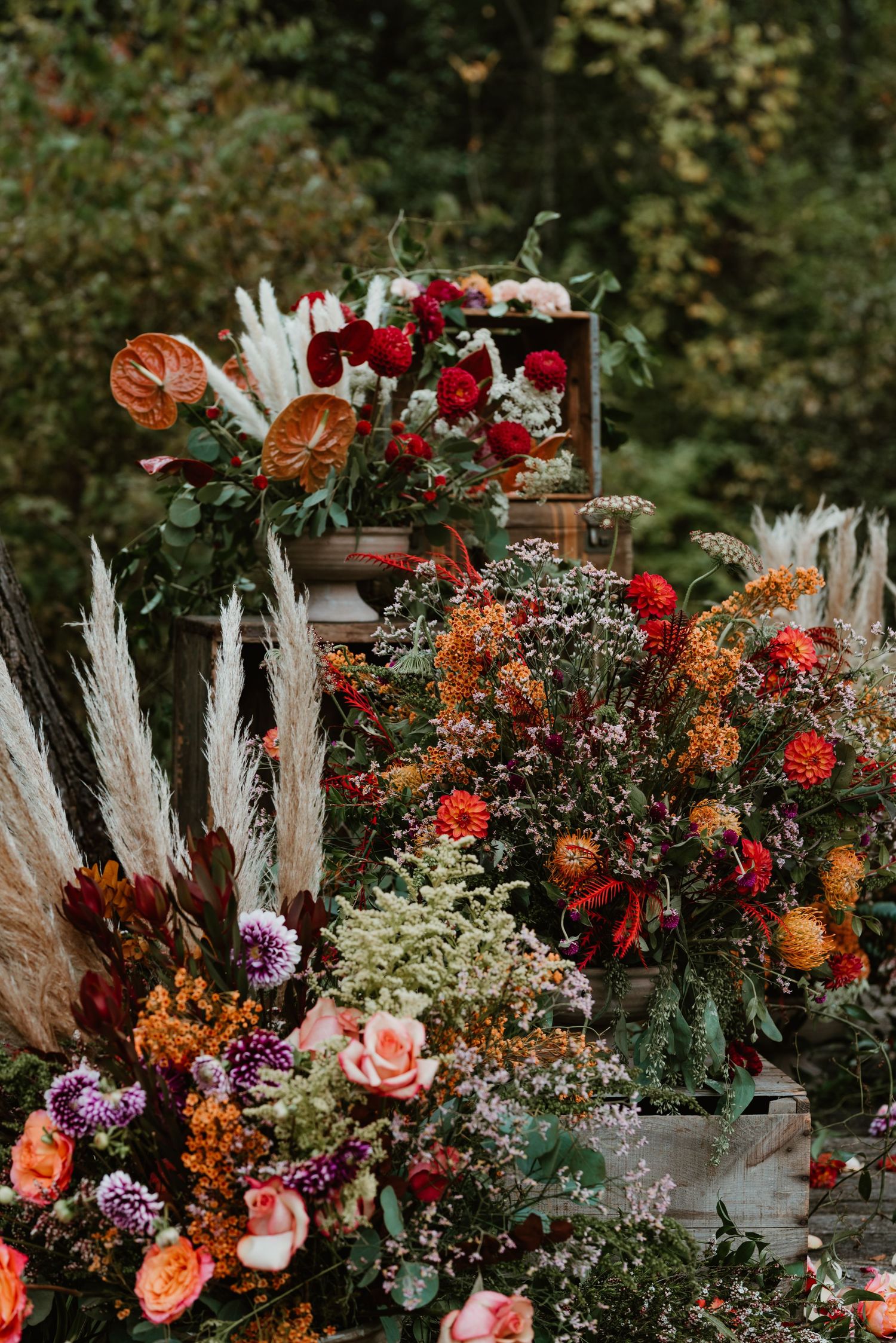 Lush fall floral arrangements with red roses, orange blooms, and pampas grass create a romantic outdoor wedding display.