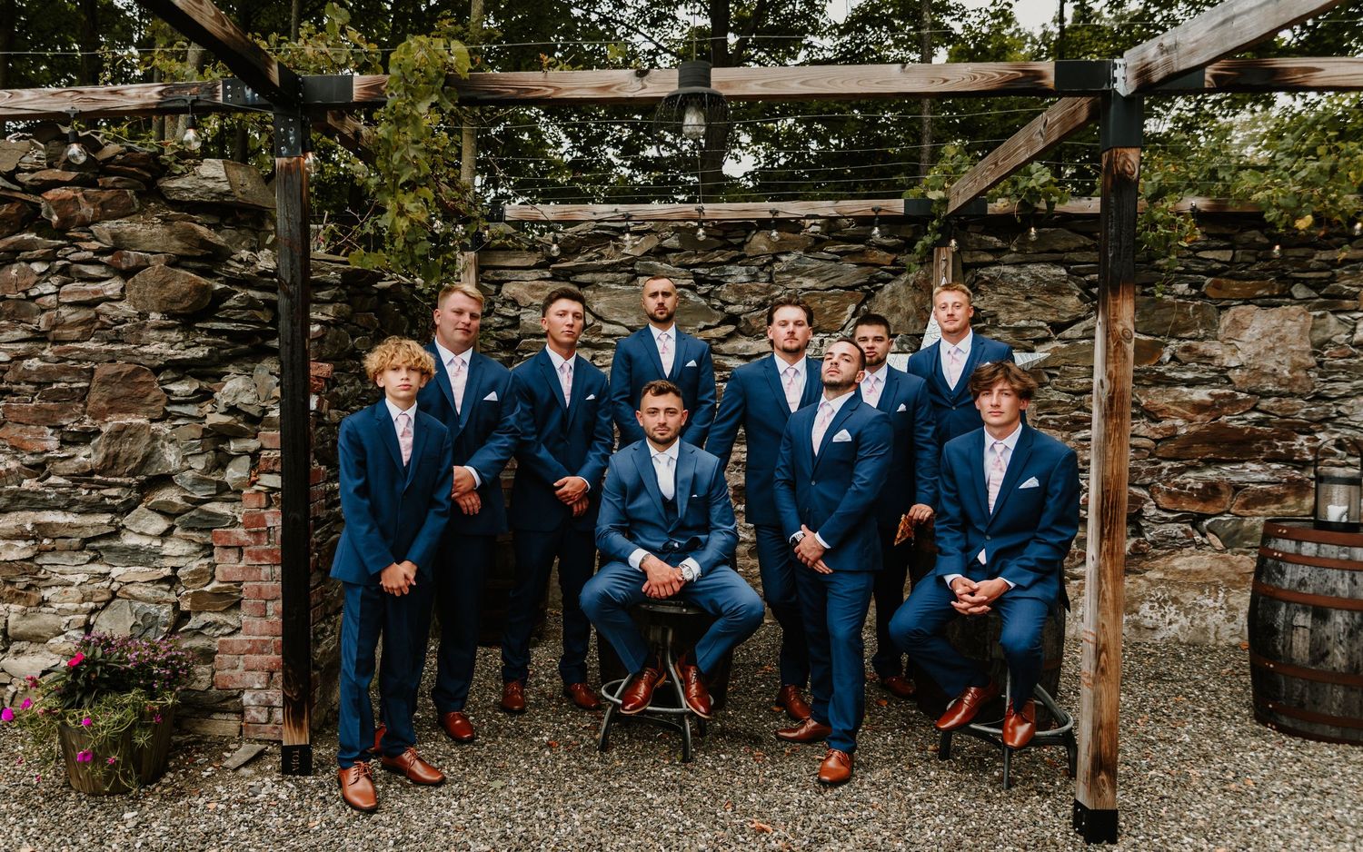 Groomsmen in navy suits pose casually on rustic stone steps during an outdoor wedding photo session.