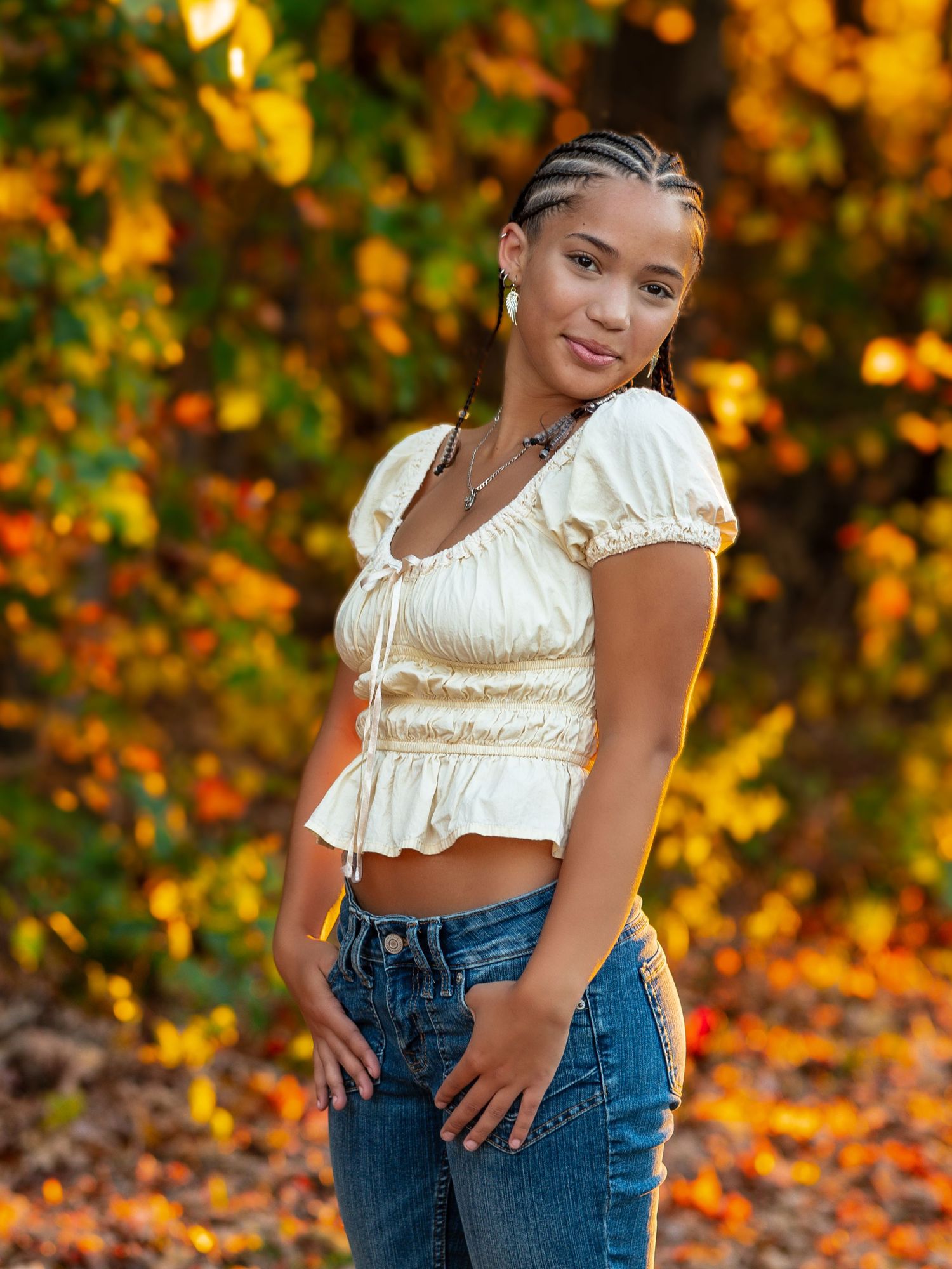 Portrait against autumn foliage wearing cream peasant top and jeans in warm golden light.