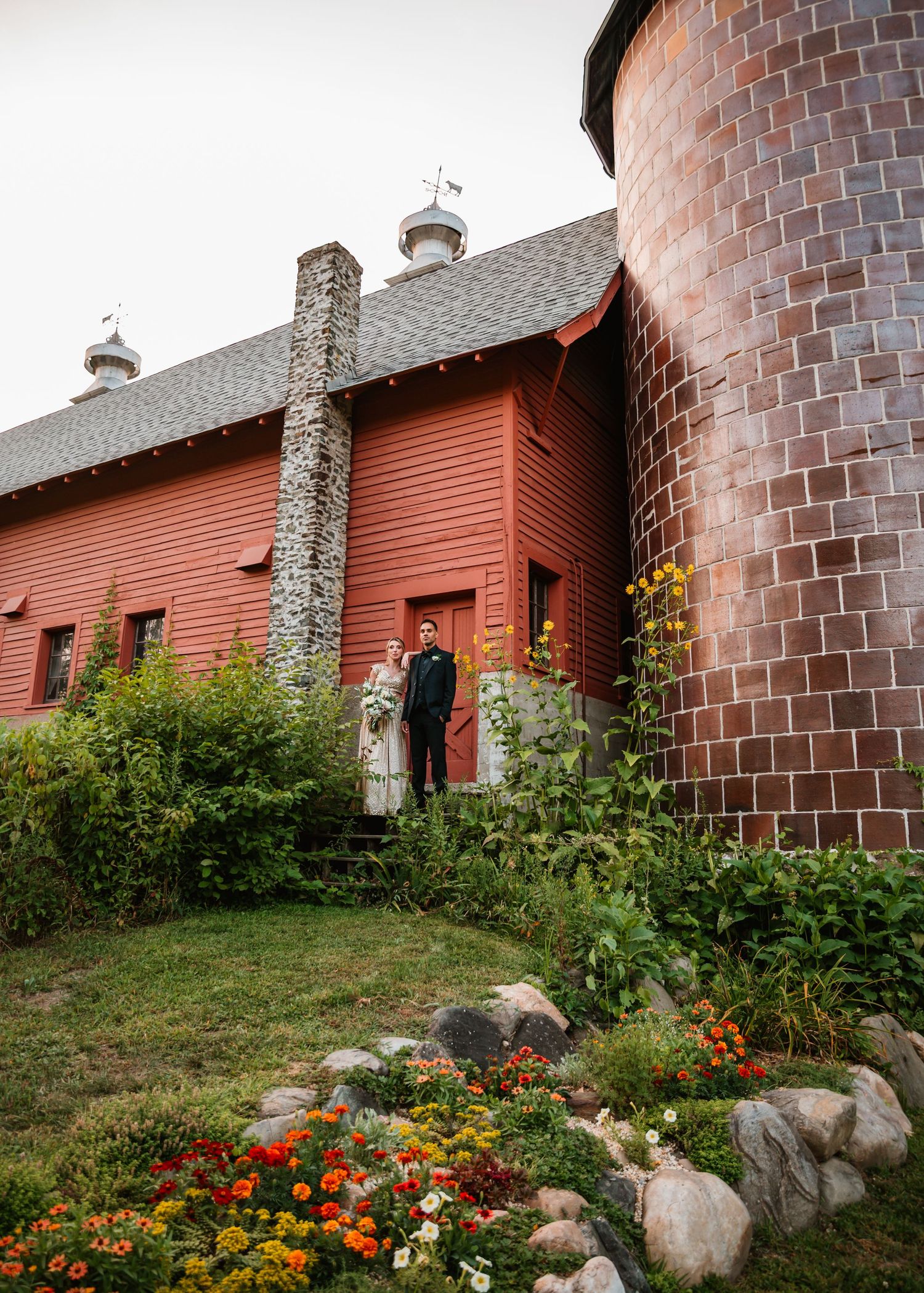 A rustic red barn with stone landscaping and colorful marigold flowers blooming in the garden bed.