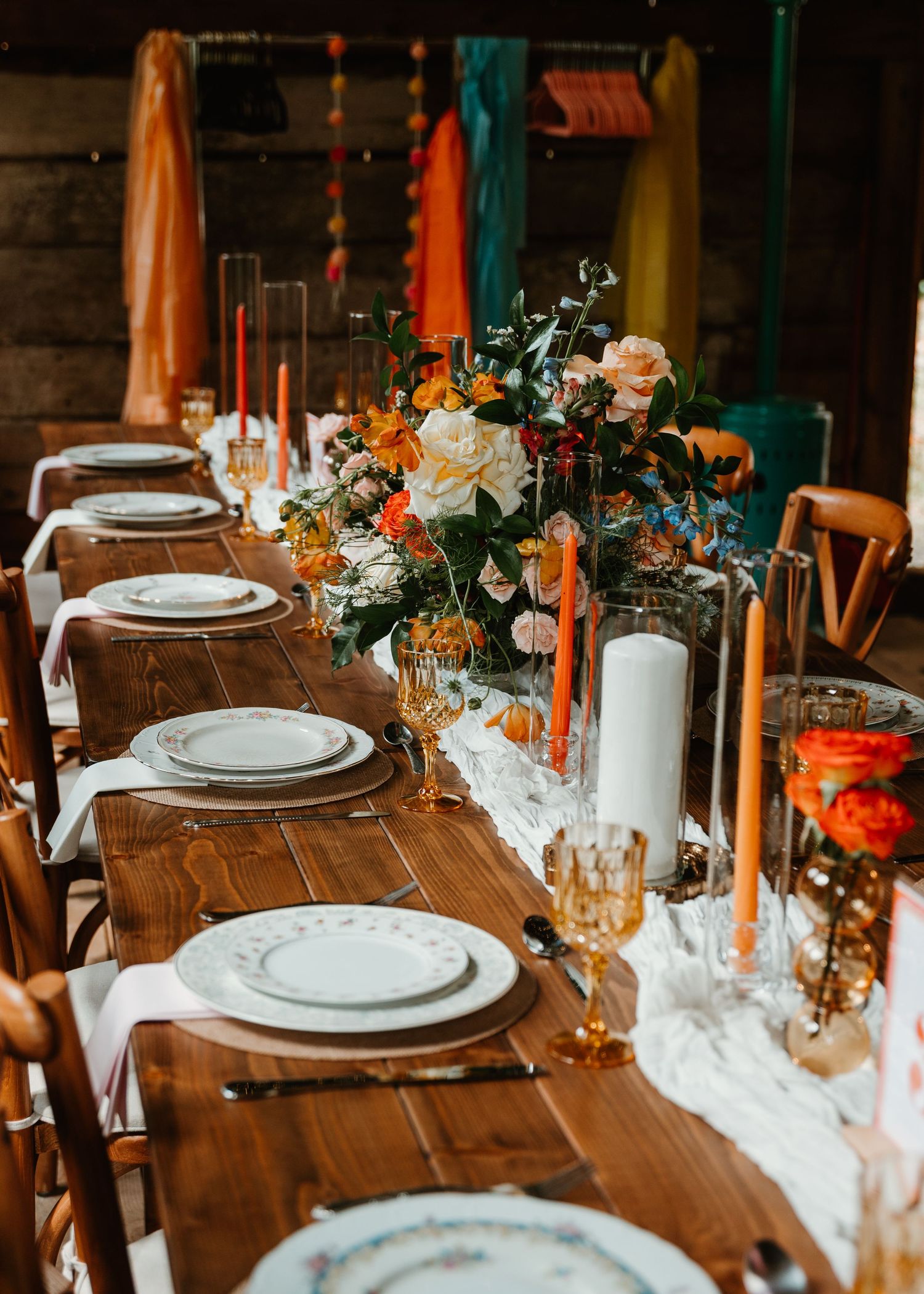 Rustic wooden dining table set with elegant place settings and orange floral centerpieces for a wedding reception.