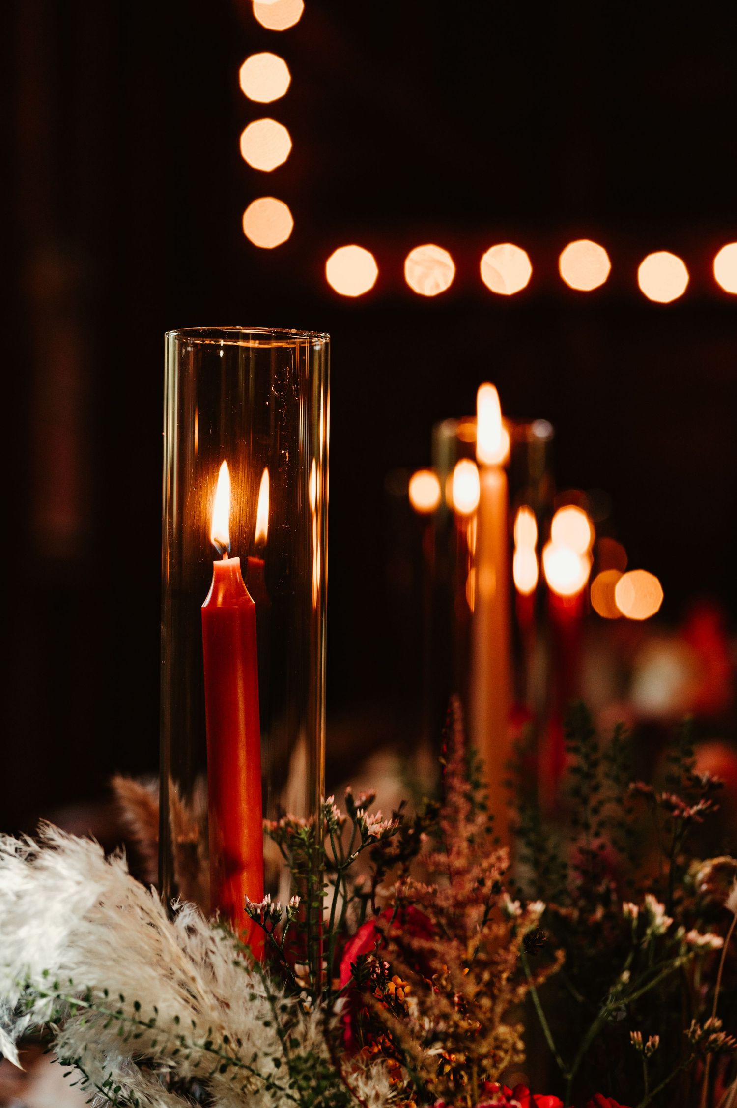 Elegant holiday table decor with red candles in glass holders surrounded by white feathers and dried flowers.